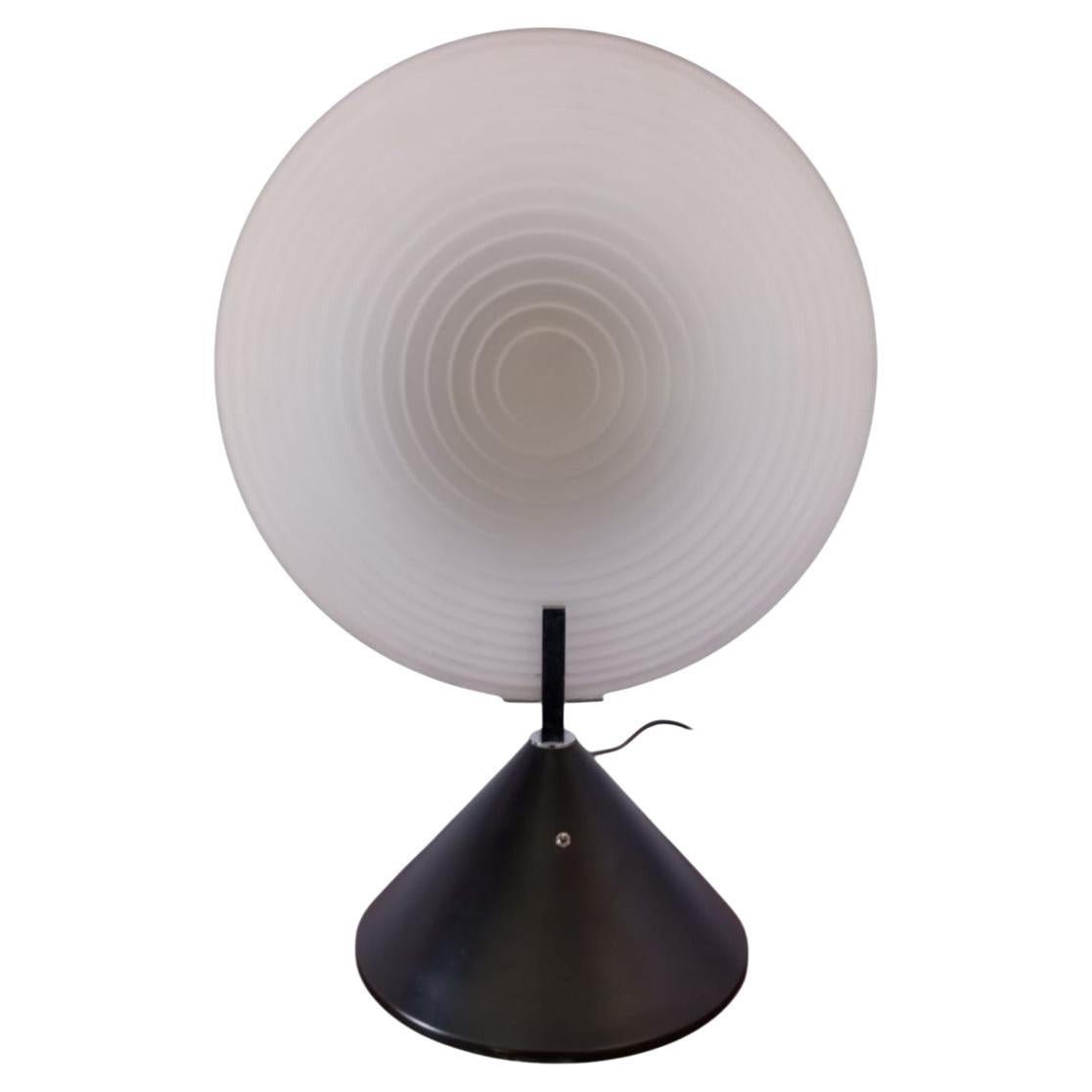 Cette lampe de table au design moderne se compose d'une base conique et d'un réflecteur, tous deux en métal noir, d'un disque diffuseur en verre opalin de Murano avec des rainures concentriques, qui contribuent à diffuser la lumière de manière