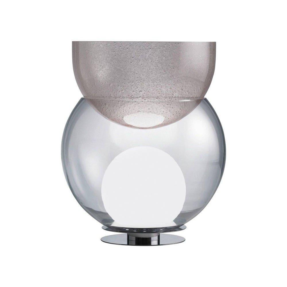 Lampada da tavolo Giova disegnata da Gal Aulenti e prodotta da Fontana Arte nel 1964. Ibrido tra un vaso e una lampada, Giova è una vera e propria scultura luminosa in vetro. Su una base in metallo è posizionato un globo trasparente in cui alloggia