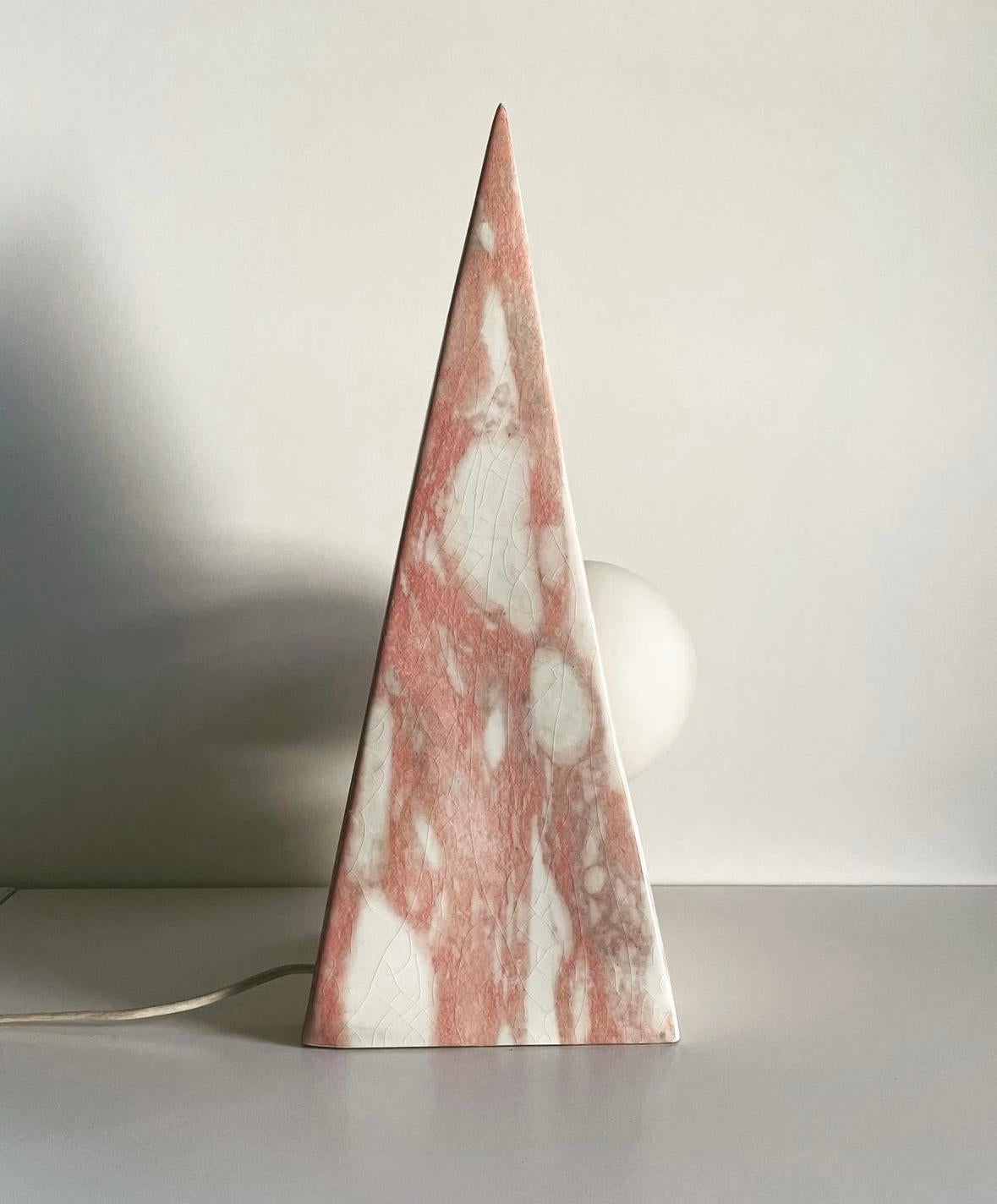 Bella e inusuale lampada da tavolo, caratterizzata da una particolare forma a piramide.
La decorazione  della ceramica è in effetto marmo, in tonalità rosa e bianche, coin finitura craquellè.   
Il corpo lumimoso, costituito da un globo di vetro