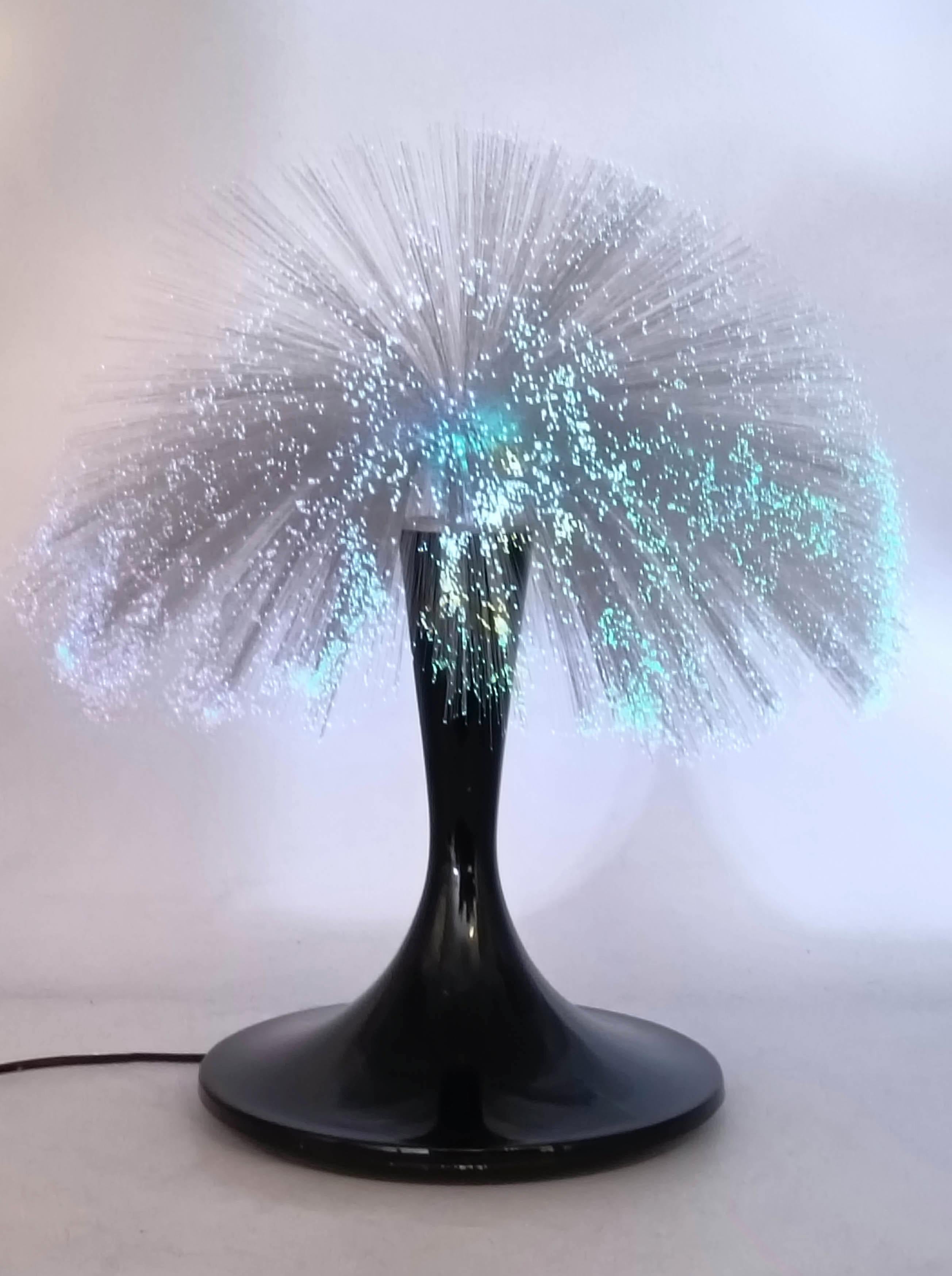 Lampada da tavolo con base in plastica nera e fili in fibra ottica che cambia colore. La lampada e' munita di telecomando per cambiare colore, intensita' e movimento