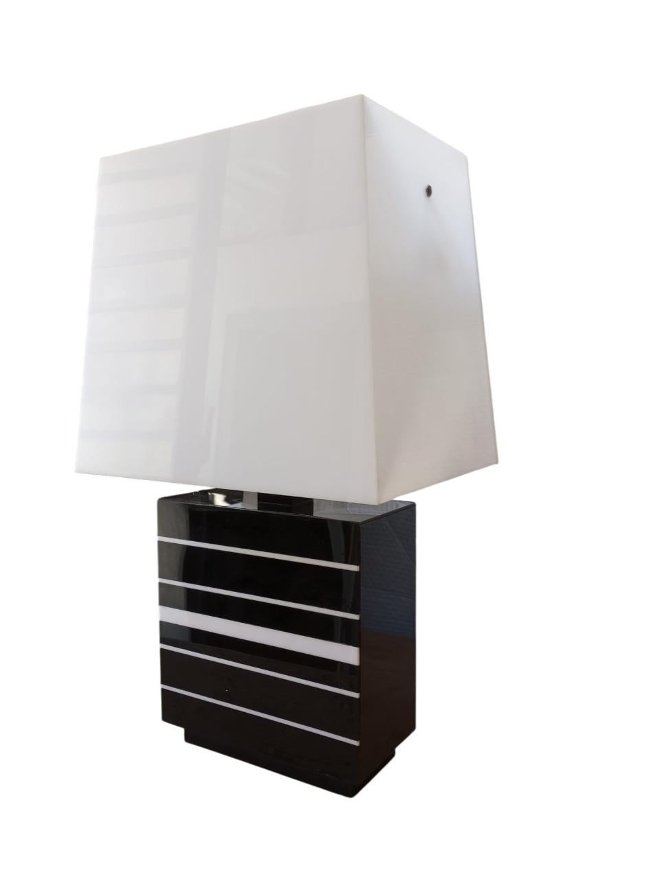 Questa è una lampada da tavolo italiana del XX secolo, dal design geometrico.
La base realizzata in lucite nera, è caratterizzata da righe orizzontali bianche equidistanti che creano un effetto grafico accattivante. La riga centrale, più larga