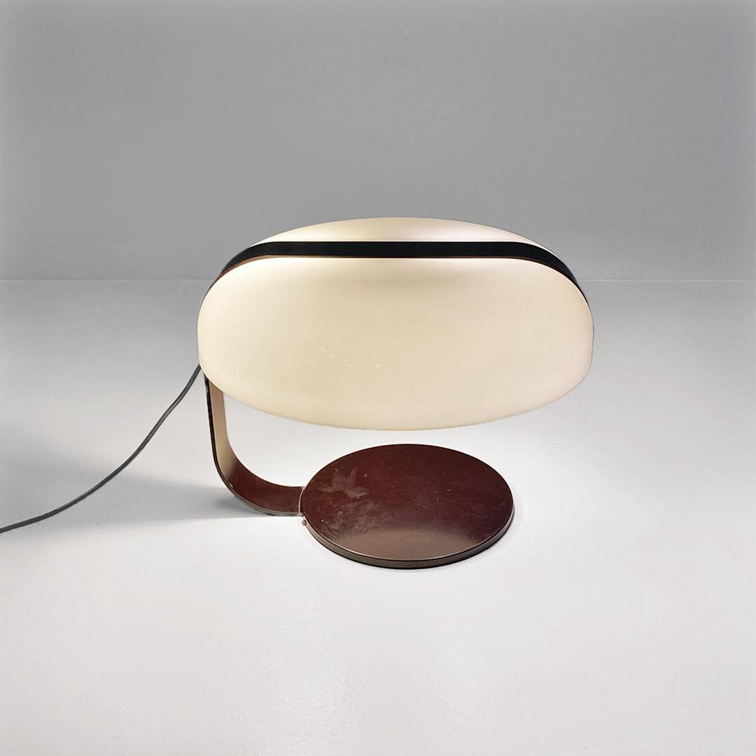 Lampada da tavolo in metallo laccato marrone e paralume stondato in perspex bianco.
Presente sulla scrivania del 