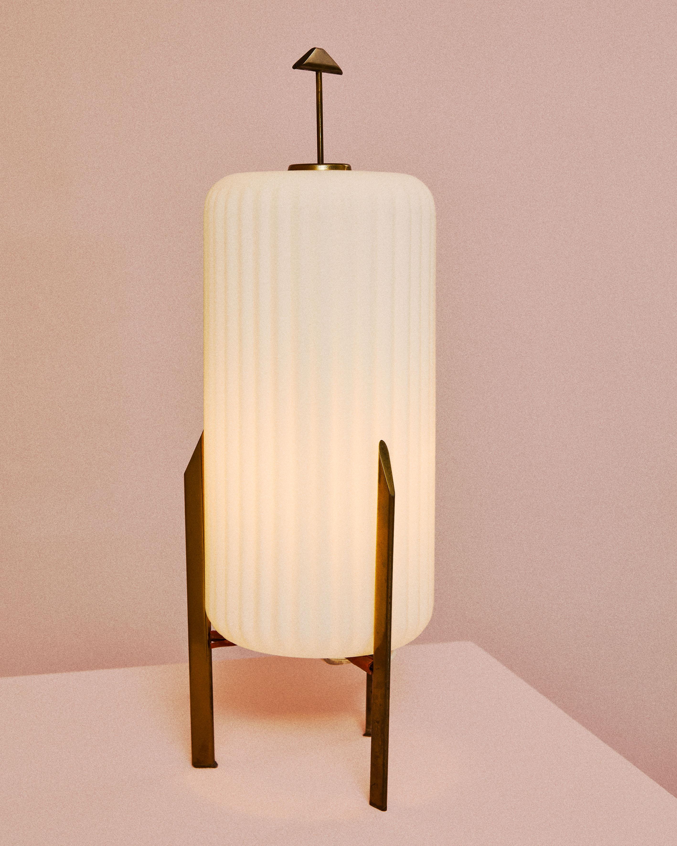 Lampe de table d'une extraordinaire élégance, caractérisée par une structure en laiton poli avec des pieds verticaux élancés et un diffuseur en verre opalin blanc travaillé avec des nervures verticales, créant un effet 