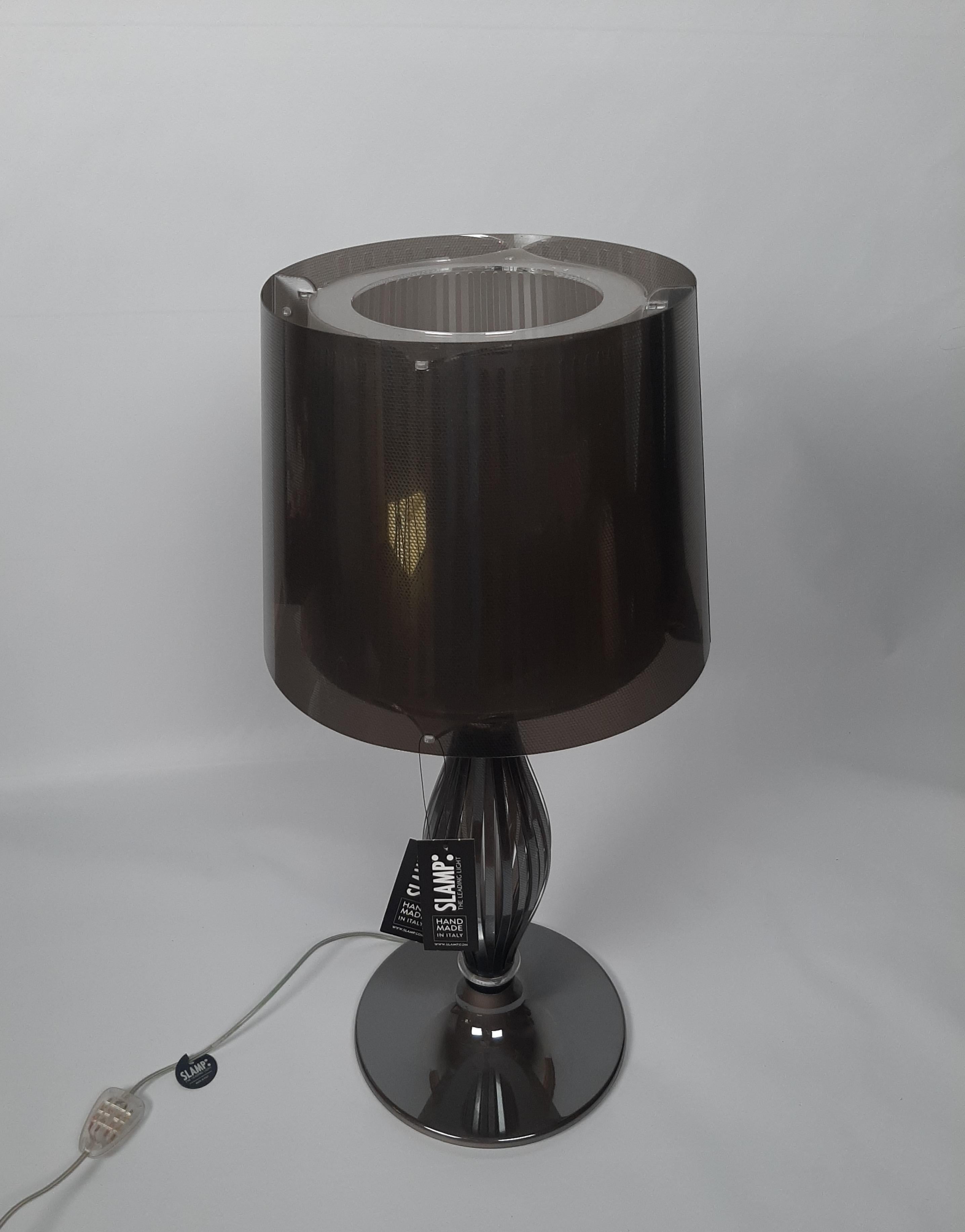 Lampe de table modèle Liza fabriquée par Slamp. Lampe modèle Liza en gris.
Lampe de table en plastique d'inspiration baroque qui combine un design à la saveur traditionnelle avec l'utilisation de matériaux contemporains, les technopolymères.
Conçue