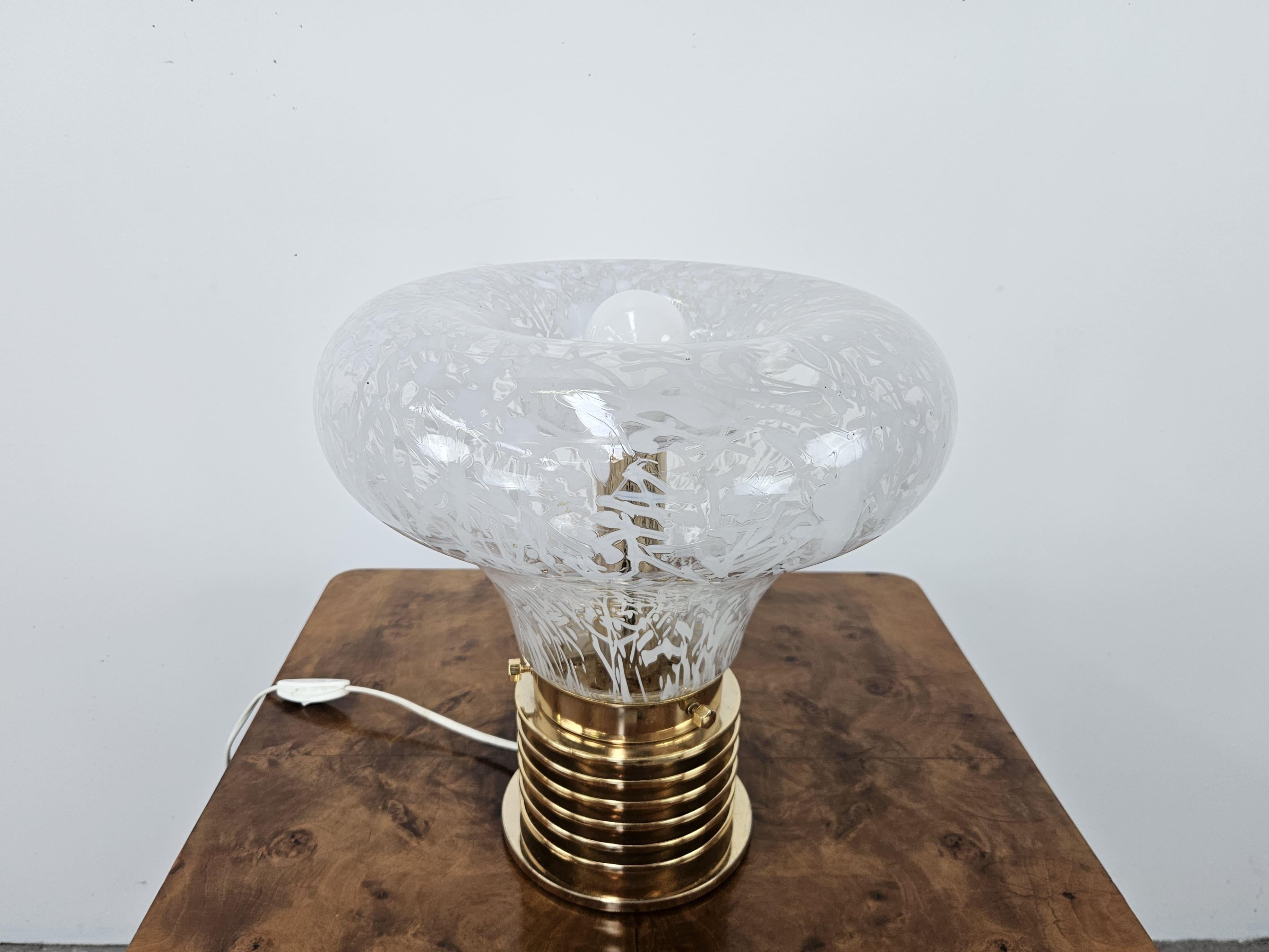 Beautiful 1970s table lamp made of worked glass with gilded metal base and exposed bulb.

Perfect for enhancing any vintage or modern setting, it lends itself to a professional studio or living room.

Original electrical system of the time.
