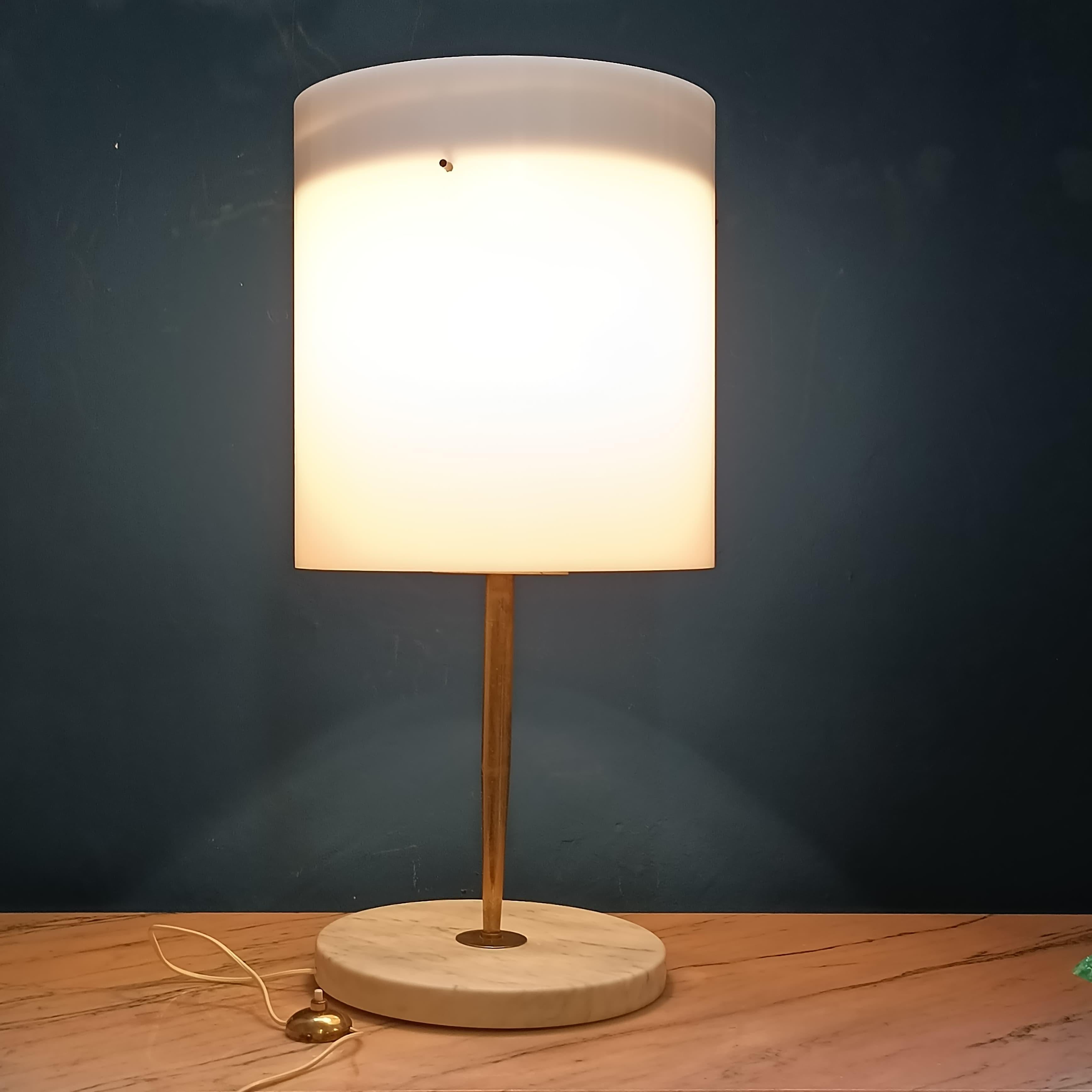 Elegante lampada da tavolo prodotta da Stilnovo negli anni '50, testimonianza del raffinato design italiano di metà secolo. Questo modello si distingue per la sua composizione materica bilanciata e per la purezza delle forme: la base rotonda in
