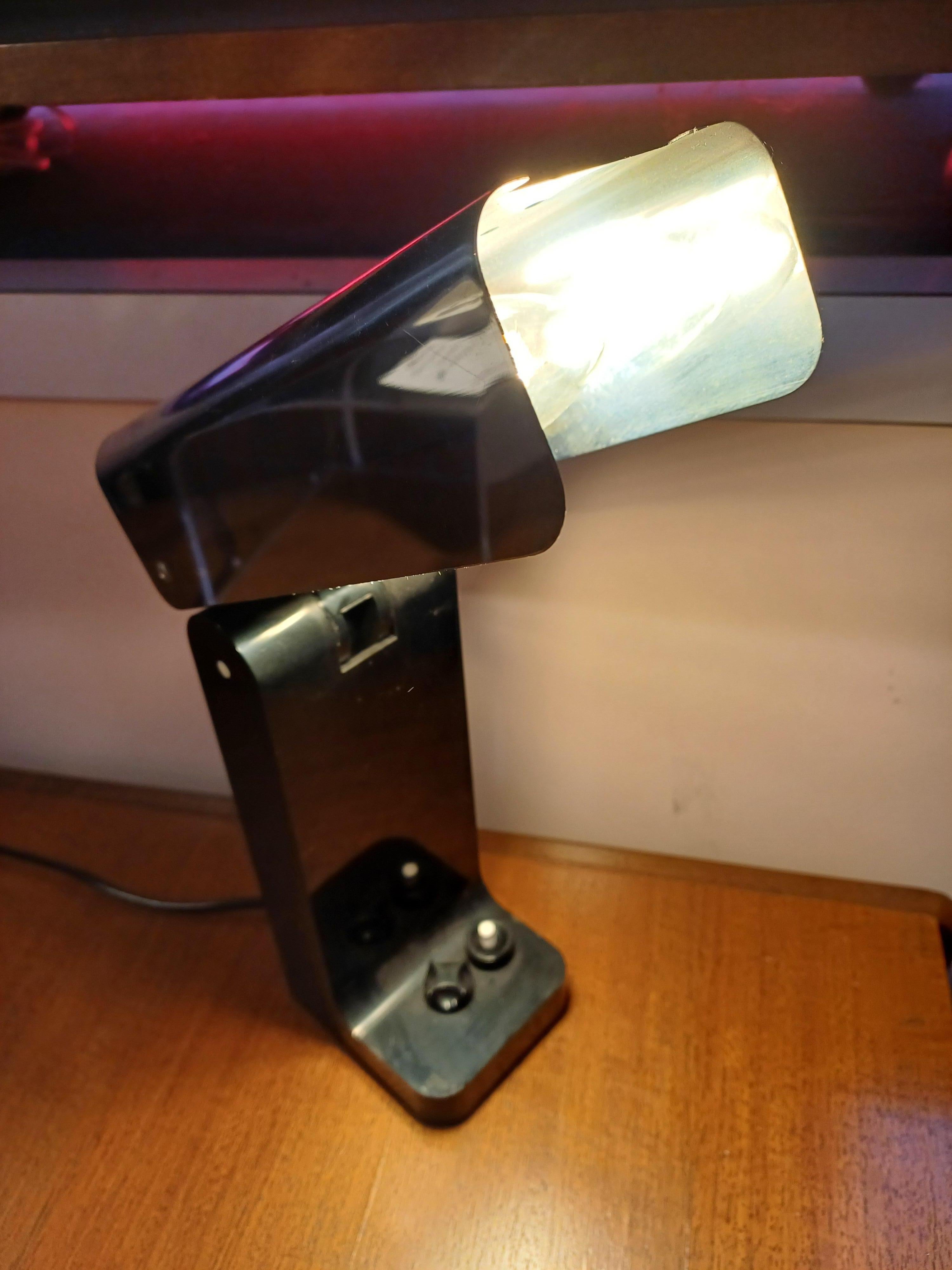 Lampada da tavolo modello Vademecum 4034 disegnata da Joe Colombo nel 1968 per Kartell Milano Italia. 
Lampada da tavolo di colore nero con paralume in acciaio inox.  Il paralume può essere chiuso. La lampada è dotata di 2 lampadine che possono