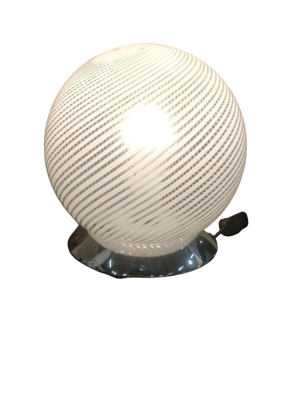 Cette lampe de table ronde de Venini est un exemple classique de l'artisanat unique et du design italien des années 1960, en verre de Murano. Il est doté d'un abat-jour en verre sphérique dont la surface est décorée de fines lignes blanches