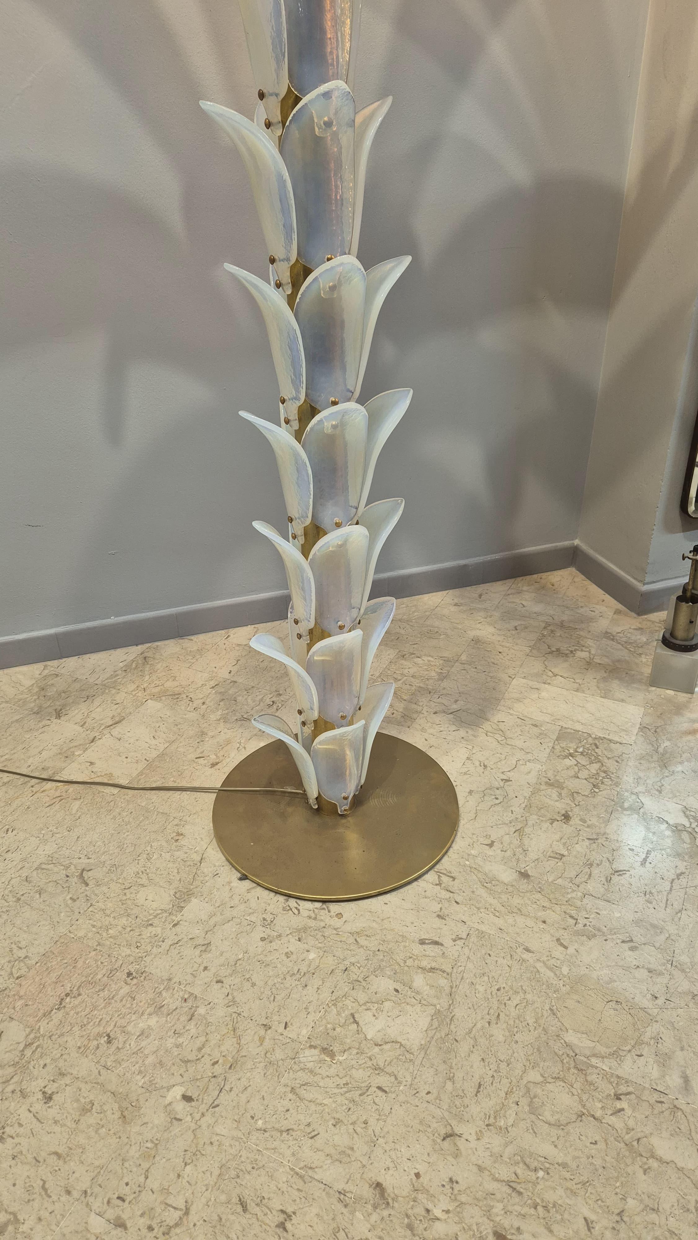 Tall floor lamp in the shape of a palm tree, consisting of a circular brass base and a trunk, covered with iridescent Murano glass leaves. At the top typical palm leaves in iridescent Murano glass.
One source of light at the top.