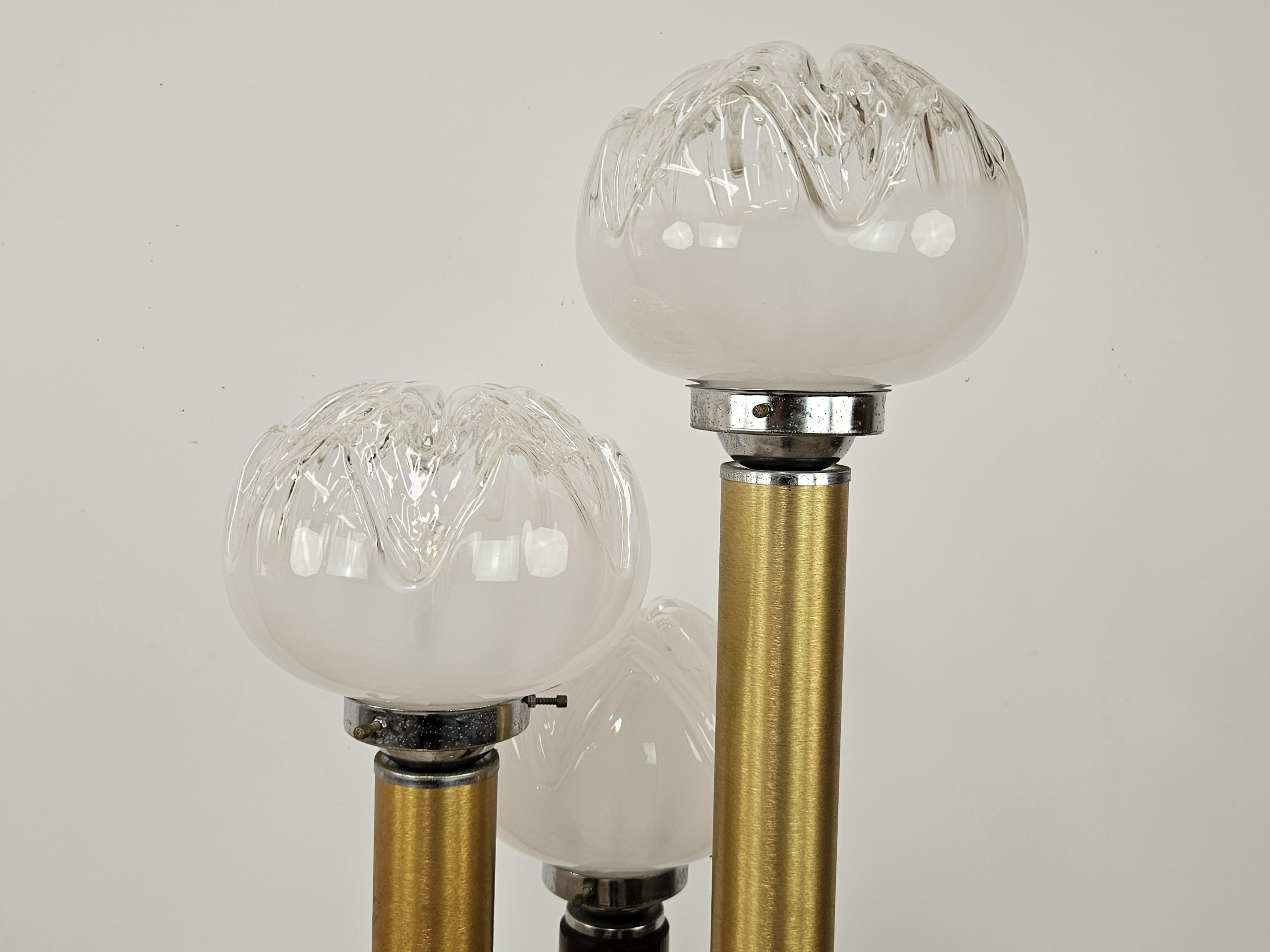 Élégant lampadaire des années 1970 avec une structure en bois et métal doré enrichie de trois points lumineux en verre de Murano travaillé dans le style du designer Mazzega.

Remarquez le lampadaire lorsqu'il est allumé, il rend tout type de pièce