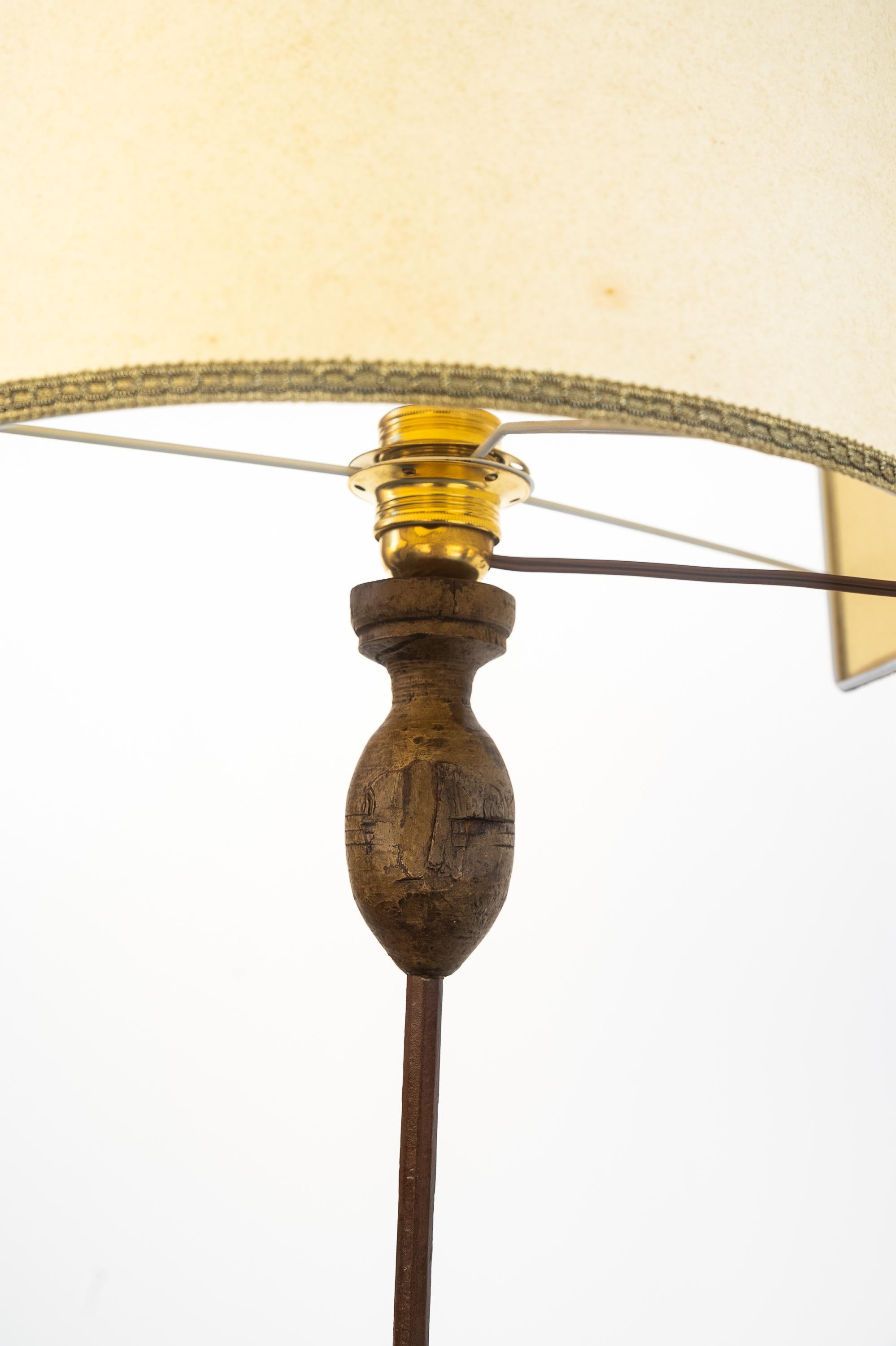 Forged iron floor lamp, early 1900s. 
Beautiful wrought iron floor lamp with four supporting legs, fixed with steel rivets. The base that holds the lamp holder is made of turned wood. In the center of the rod is an iron ornament. The wiring has been