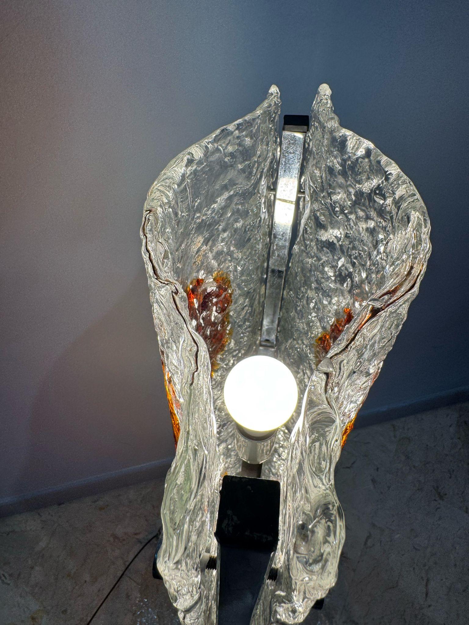 Questa è una straordinaria lampada da terra prodotta da Mazzega negli anni ’70, un autentico esempio di design italiano che fonde arte e funzionalità.
La struttura è caratterizzata da lastre di vetro di Murano lavorate a mano, con una superficie