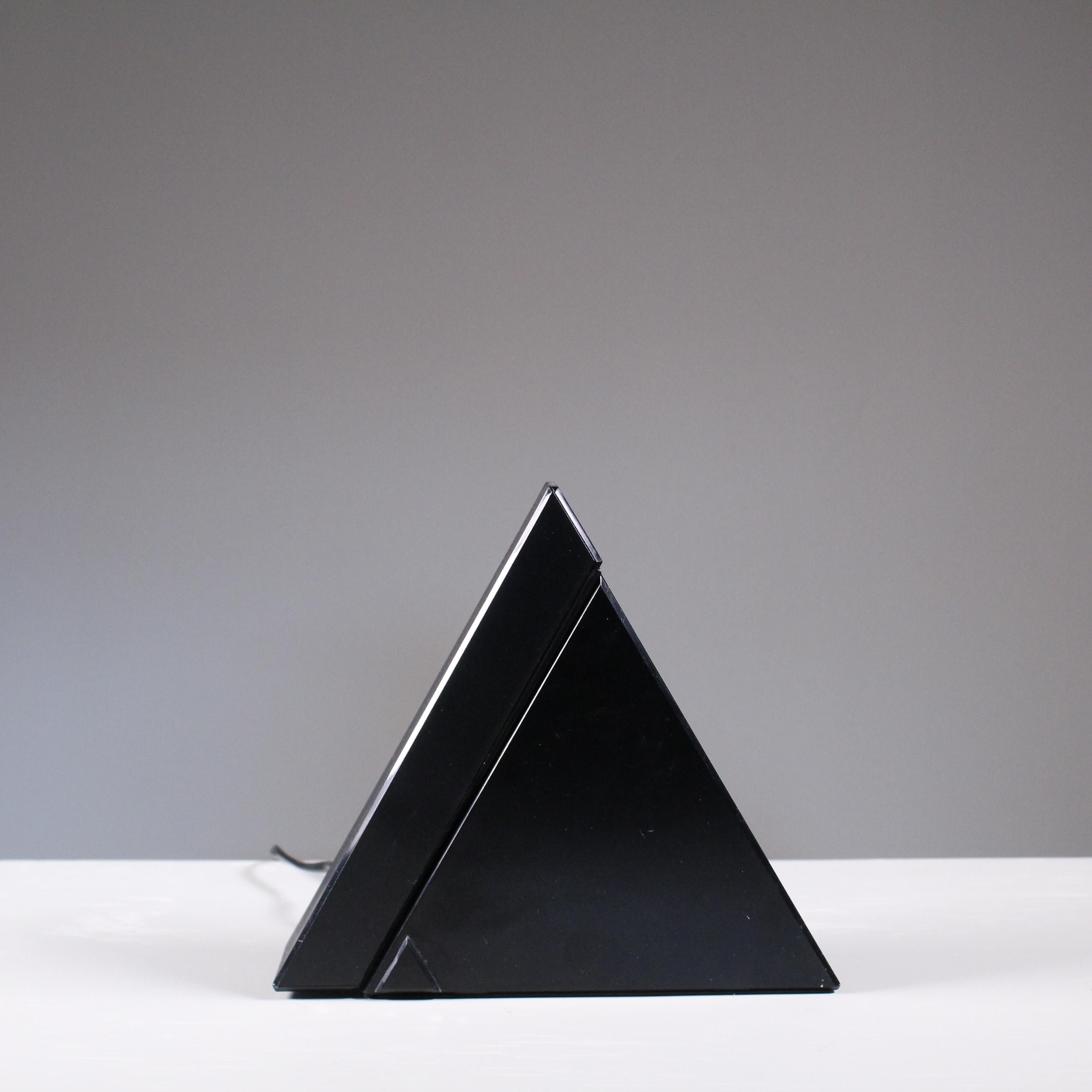 Lampada da tavolo disegnata da Mario Bertorelle per JR RDM nel 1980. Caratterizzata da un design geometrico e pulito, Delta riflette lo stile industriale e funzionale del periodo, con una struttura in plastica nera e diffusore orientabile. Un pezzo