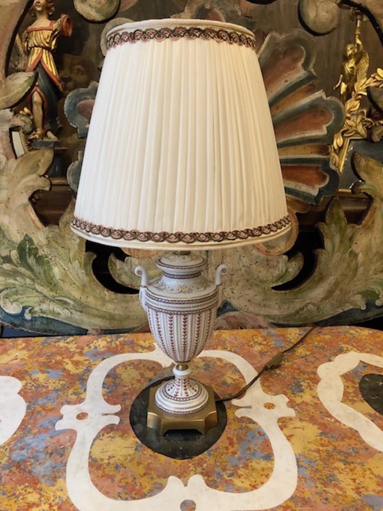 Lampada da tavolo fiorentina vaso a forma di urna dipinto a mano dalla ditta italiana Mangani di Firenze di gusto neoclassico, con volute e dettali floreali dipinti in oro, manici e base sagomata in bronzo dorato. La decorazione policroma in verde e