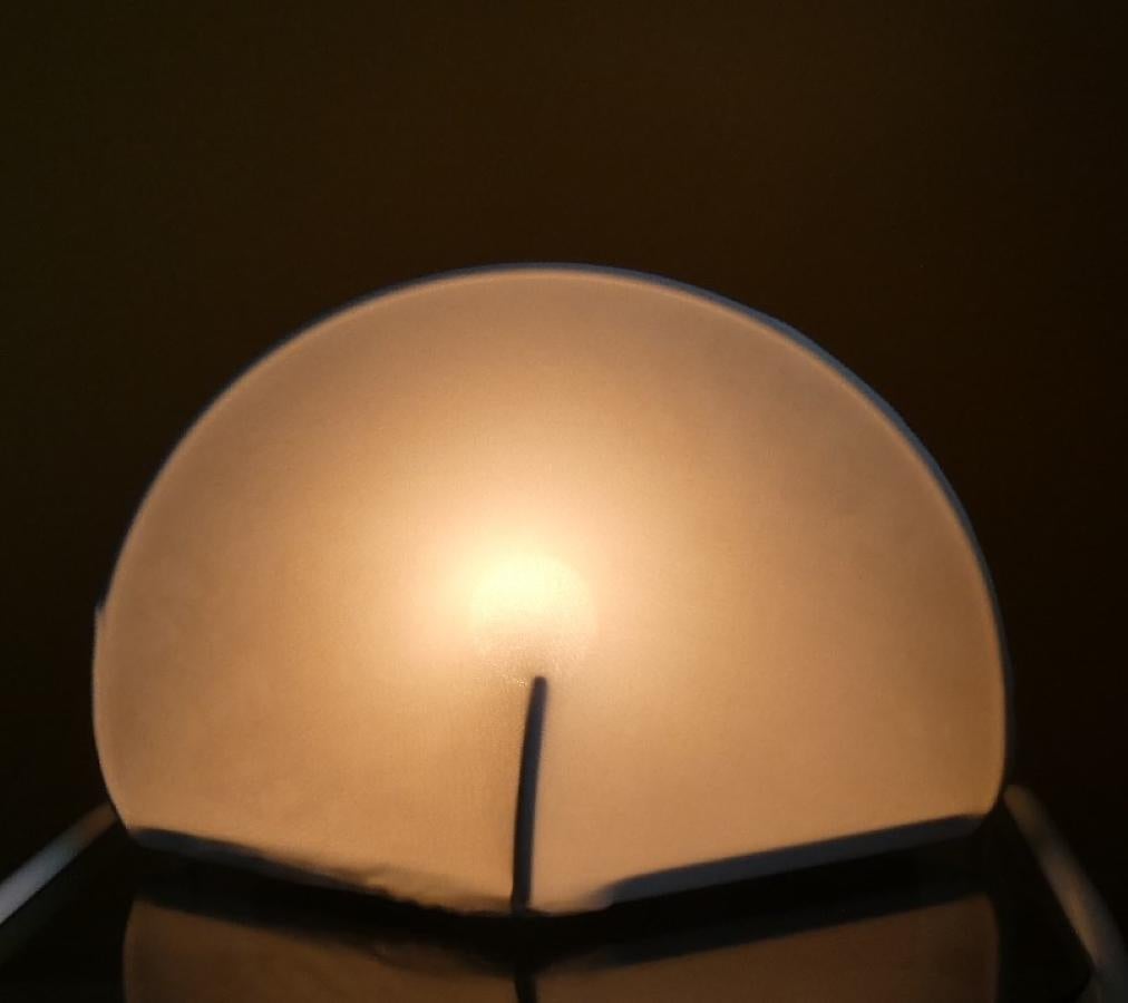 Lampada Kaori  in tessuto elastico. Può essere utilizzata si come lampada da tavolo poichè dotata di piedini in gomma antiscivolo, oppure sfruttata come applique dato che sulla parte posteriore è presente l'apposito gancio. Condizioni eccellenti.
