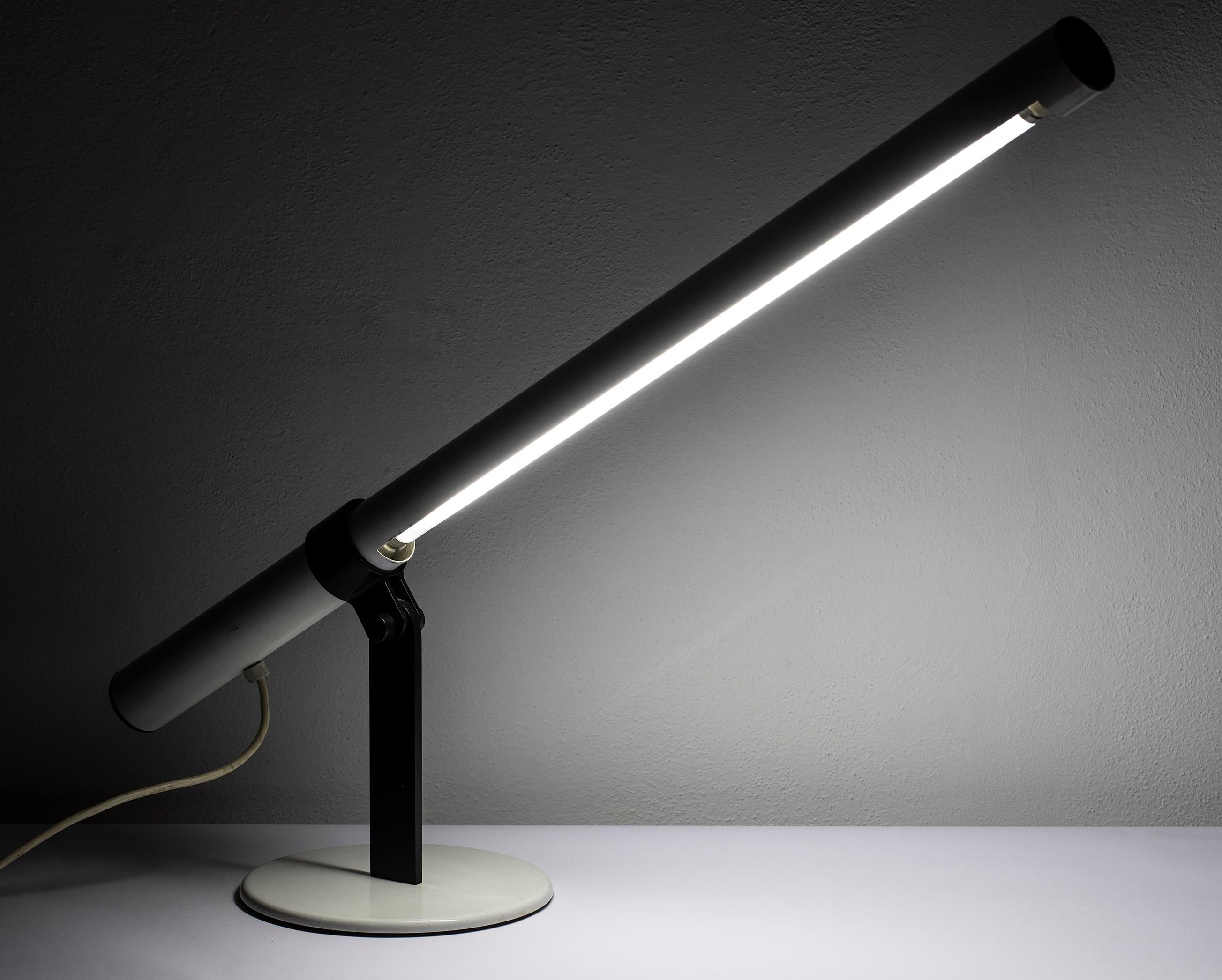Particular neon lamp, produced in Italy in the 1970s. It features a metal chassis lacquered in shades of white, containing a neon tube; the structure is tilting and adjustable and rests on a metal base lacquered in black. Presents some minor