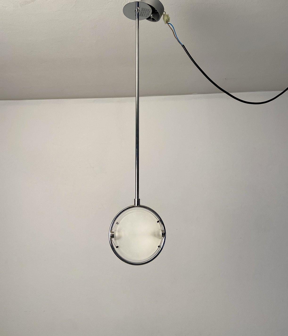 Lampada a sospensione Nobi Mod. 3023/1 disegnata da Metis Lightning e prodotto da Fontana Arte in Italia nel 1992. Con uno stelo in acciaio lucidato a lunghezza fissa, la lampada si compone di una fonte luminosa circolare, formata da due vetri