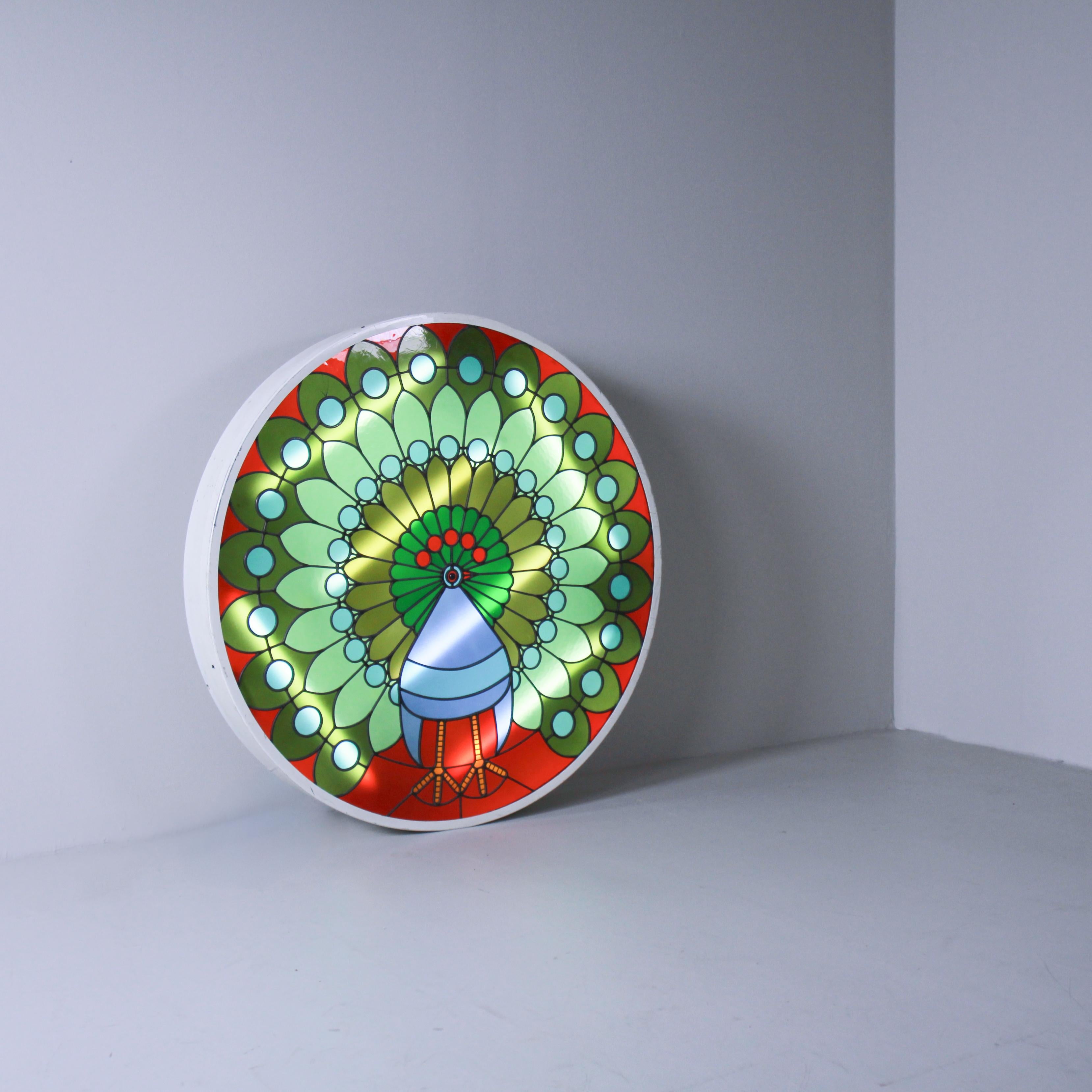 Ce plafonnier de 1970 présente une illustration naturelle d'un paon coloré. Réalisé en métal et en plastique, il combine un graphisme détaillé et vivant avec une structure élégante qui fait de l'objet non seulement un point de lumière mais aussi une