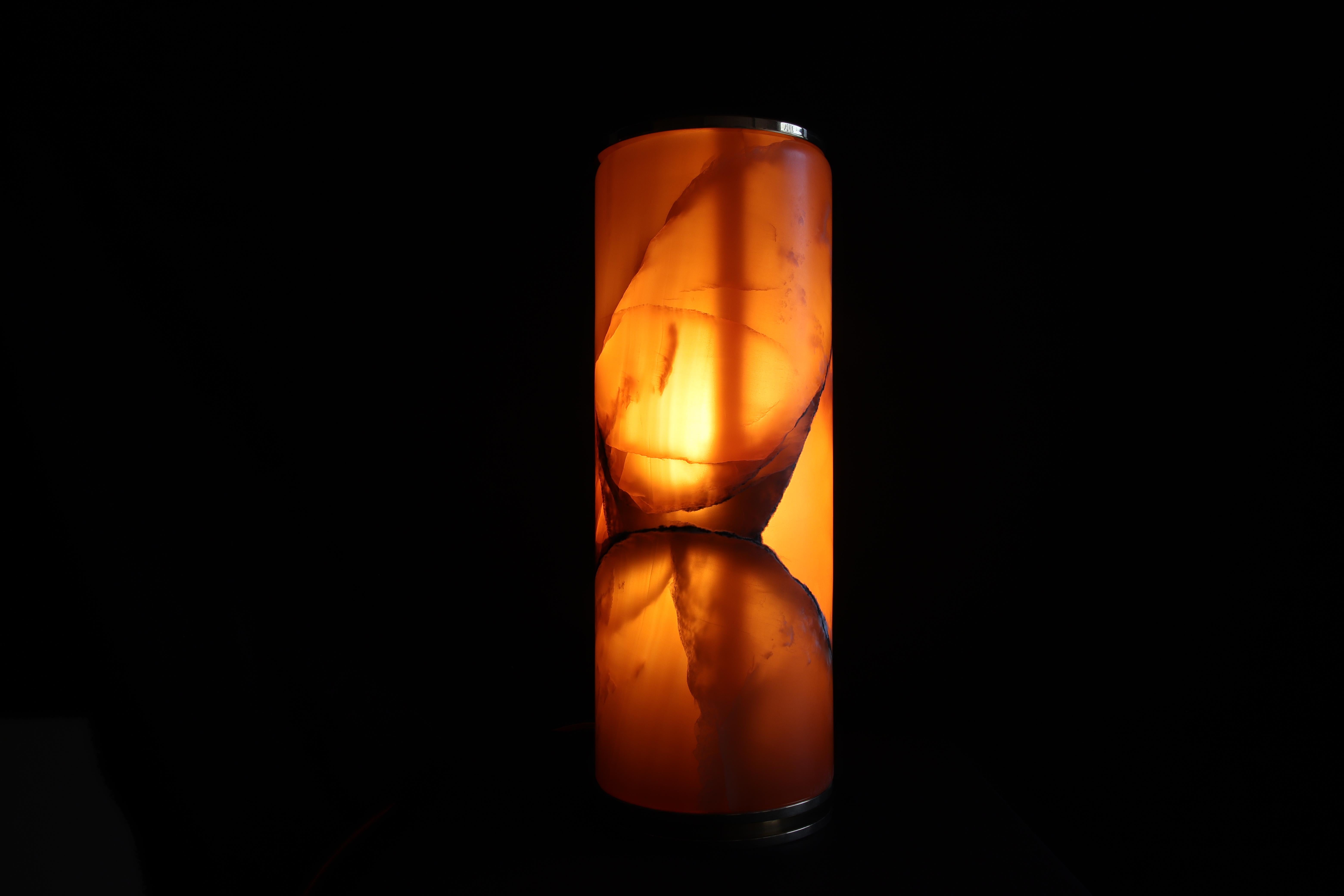 La lampada Superba è realizzata in onice ambra, bronzo ed ottone. Essenziale nel design per esaltare la rara bellezza di questa pietra naturale semitrasparente. Il fondo è di un colore ambra caldo, ed è attraversata da nuvolature più chiare che con