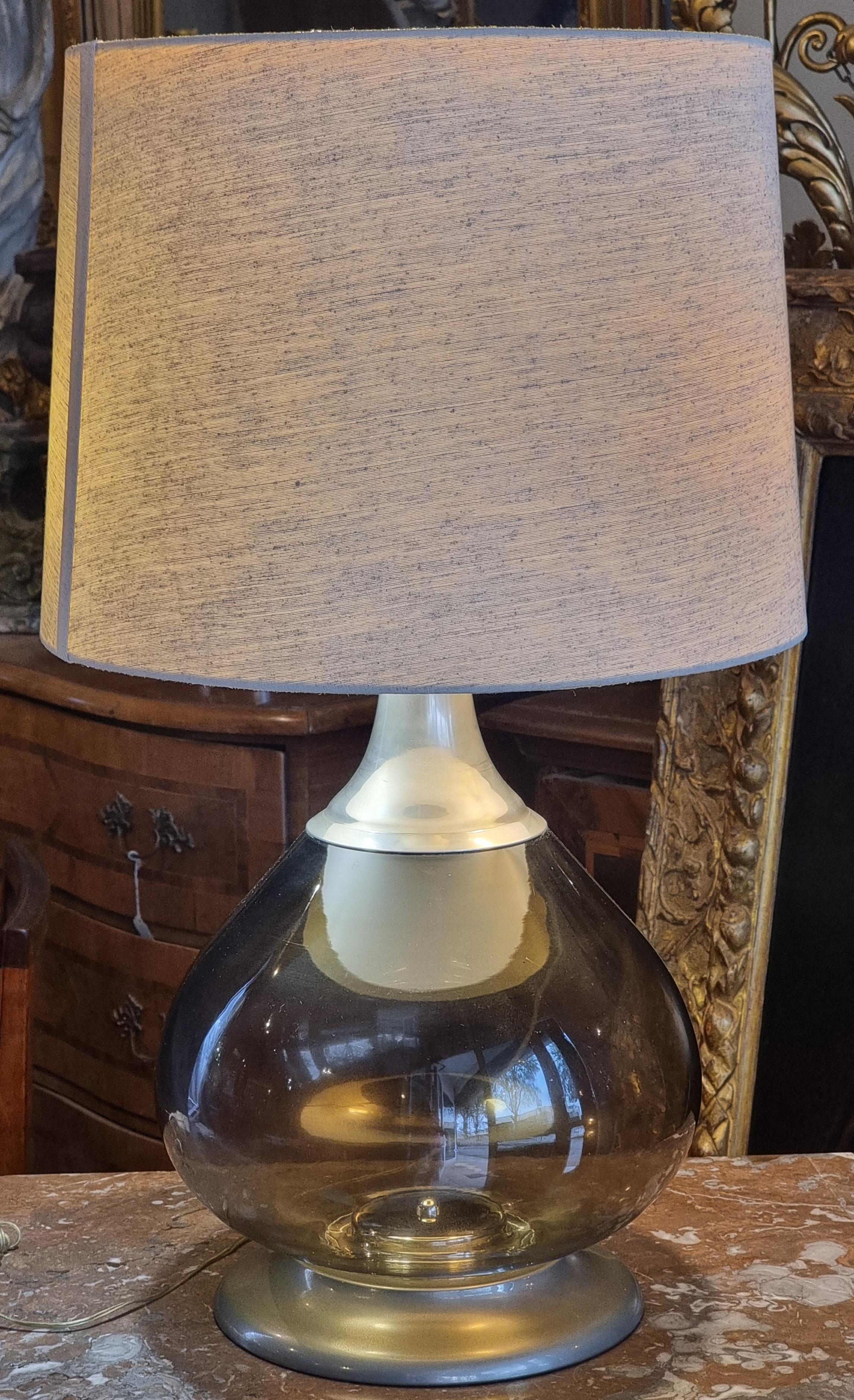 Important lampadaire de la région de Murano, datant des années 1970. Le corps est constitué d'une grande bulle en verre fumé soufflé (Ø environ 34,5 cm) sur une base et un collier en métal argenté, avec un système électrique coexistant. L'ensemble,