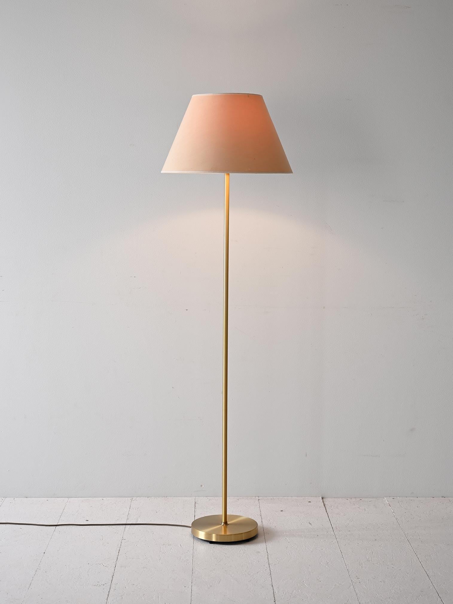 Lámpara de pie escandinava con tija de metal dorado y pantalla cónica de tela. 

La base circular estable y el tallo delgado aportan ligereza visual, mientras que la pantalla difunde una luz cálida y suave, perfecta para crear un ambiente acogedor