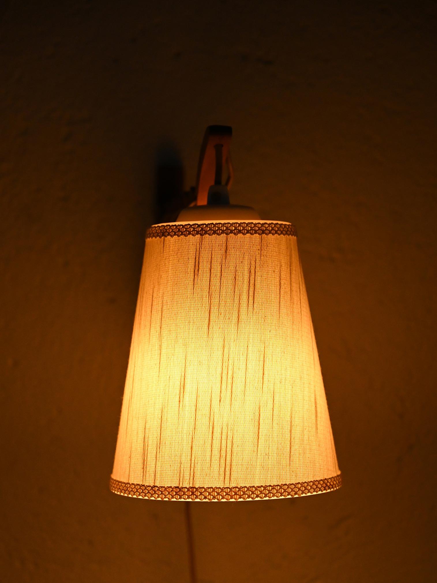 Aplique de estilo retro con brazo extensible (longitud máxima 78 cm)  madera y pantalla cónica de tela.

La pantalla es cónica, revestida de tela beige claro, con un motivo decorativo muy sencillo y delicado en los bordes. El marco de madera, con su