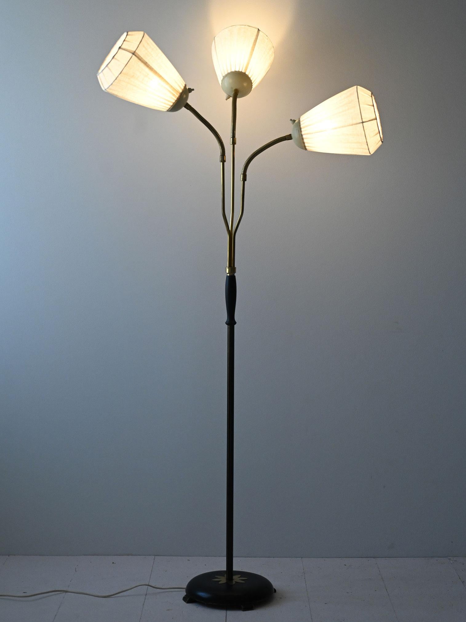 Vintage floor lamp featuring a black metal frame and brass details, giving it an elegant and sophisticated look. The sturdy circular base features a golden star motif.
The three flexible brass arms end in pleated white fabric lampshades, which