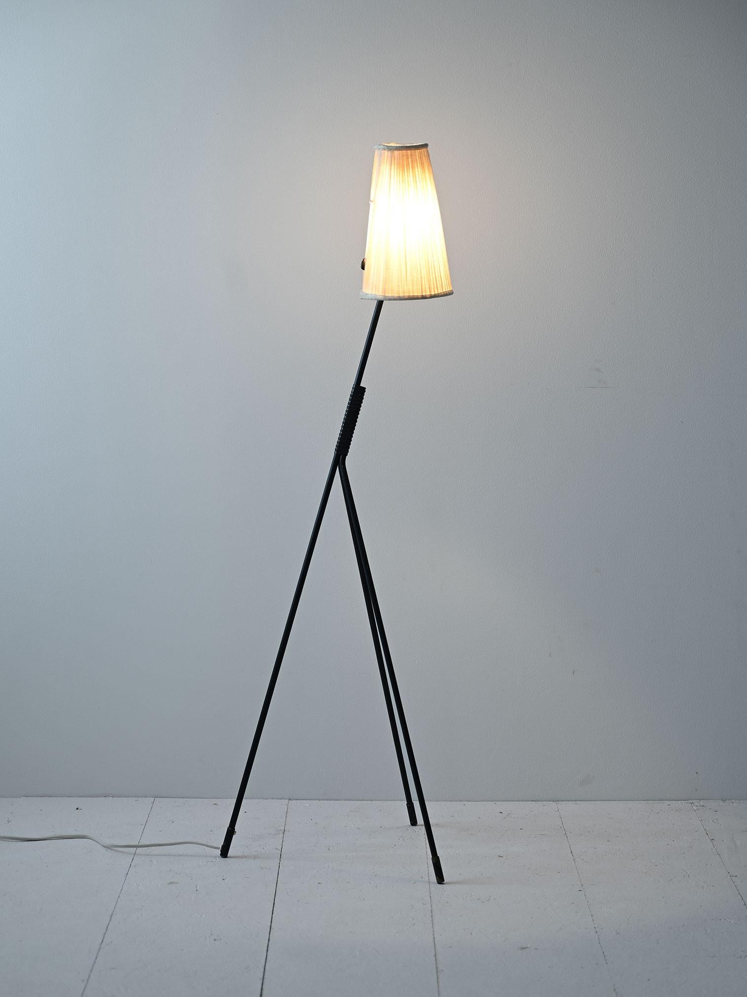 Esta lámpara vintage presenta un diseño distintivo con un tallo formado por tres pies metálicos pintados de negro. El contraste entre el metal oscuro y la pantalla cilíndrica de tela crea una elegante combinación de modernidad y clasicismo.

El