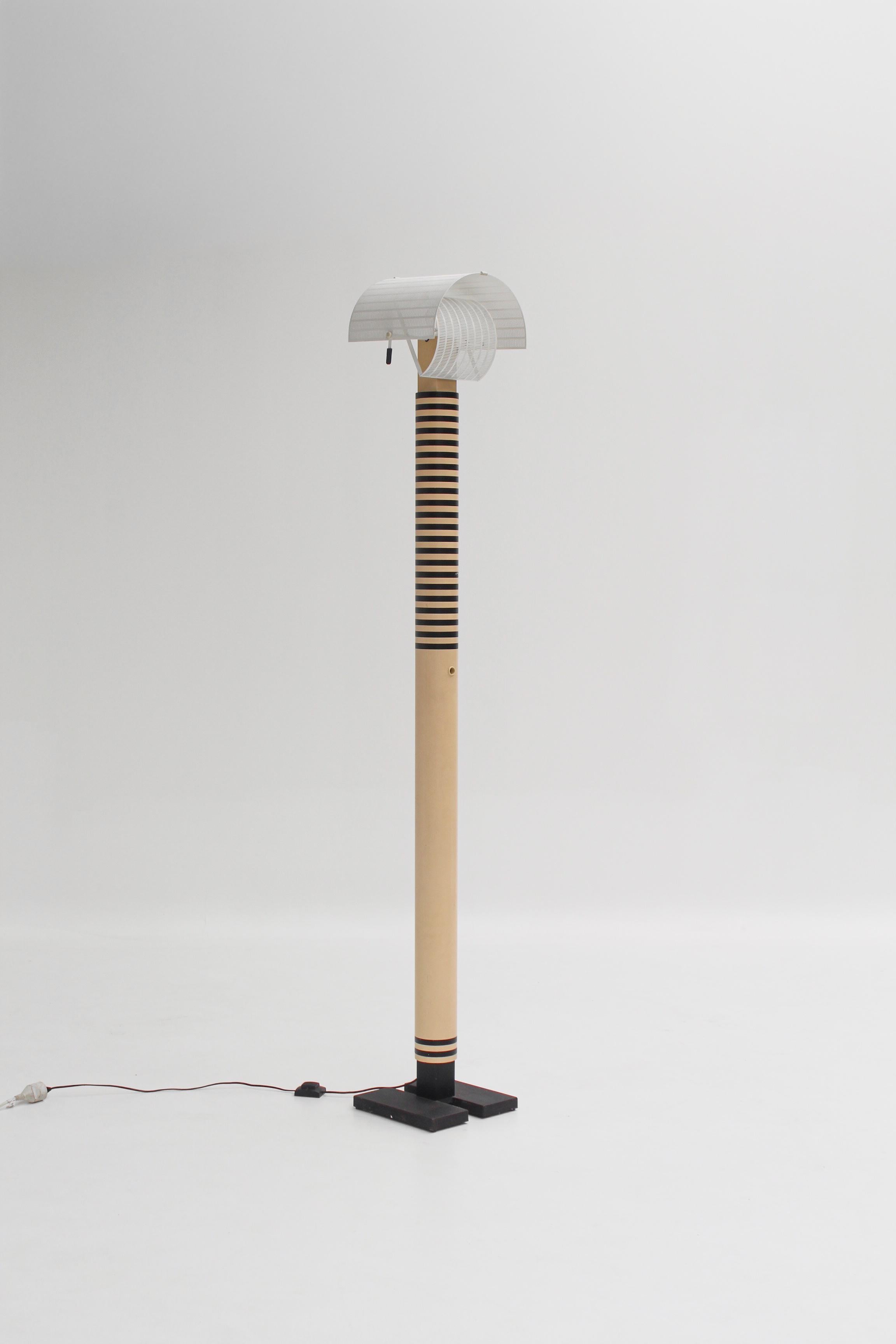 Icône du design postmoderne italien, le lampadaire Shogun a été dessiné par Mario Botta pour Artemide en 1986.
Reconnaissable entre mille par son abat-jour en tôle perforée orientable, il joue sur la lumière et l’ombre à travers un maillage