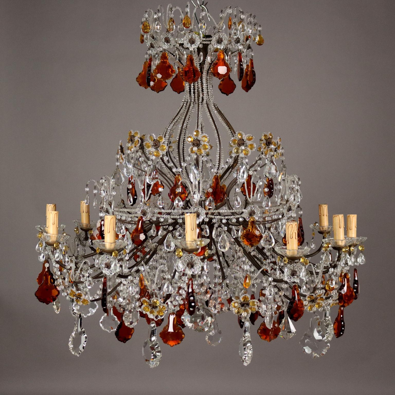 Twelve-light chandelier in burnished metal, richly adorned with necklaces, bobeches, pendants, waterfalls and flowers in glass and stained glass.
Italy, early 20th century.	