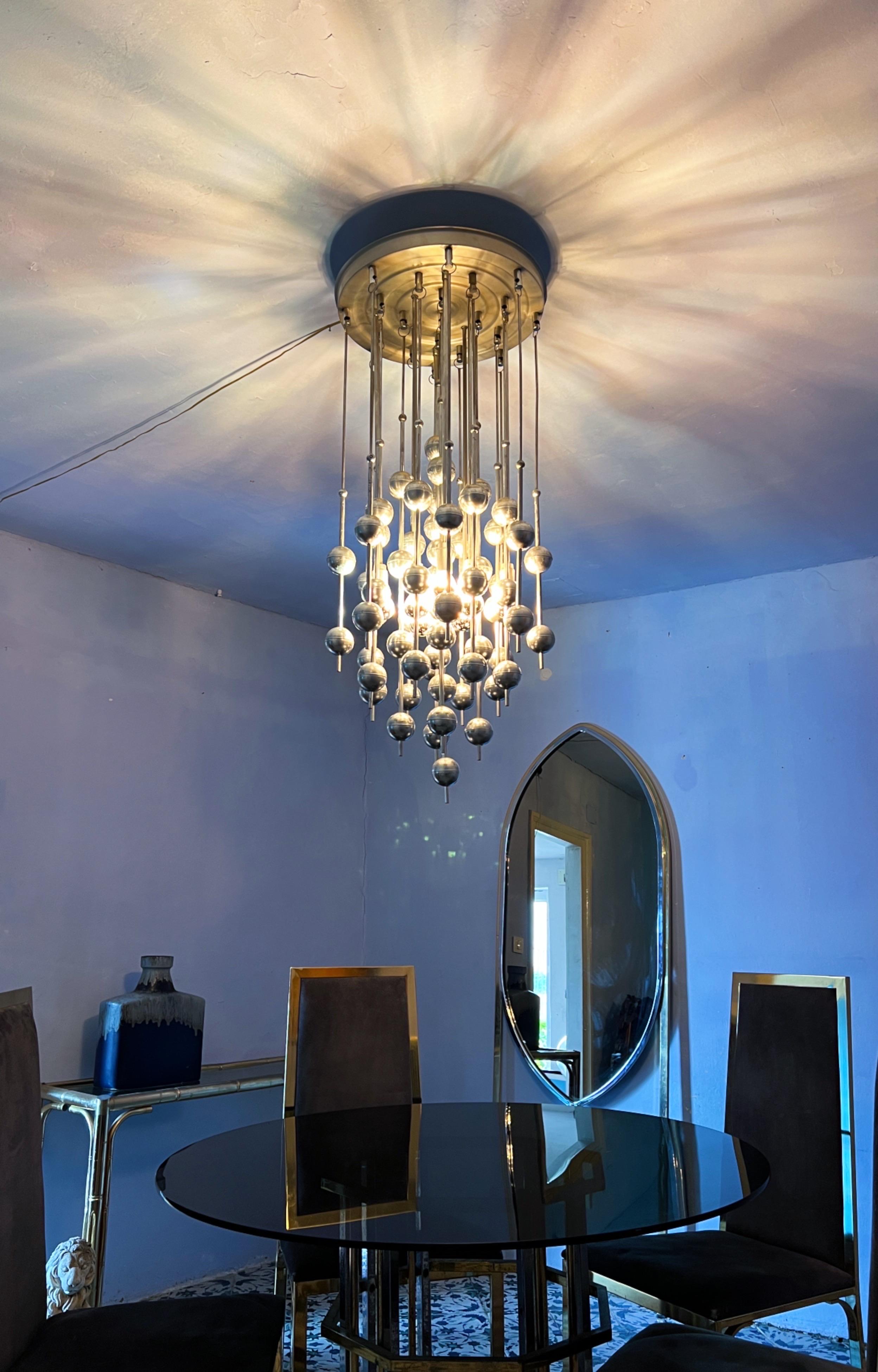 Let me introduce: the Amazing Chandelier, envisioned by the acclaimed Danish designer Verner Panton for J. Lüber during the illustrious 1970s era. Suspended with grace from steel rods, there are 21 chromed straws adorned with metal balls. With its