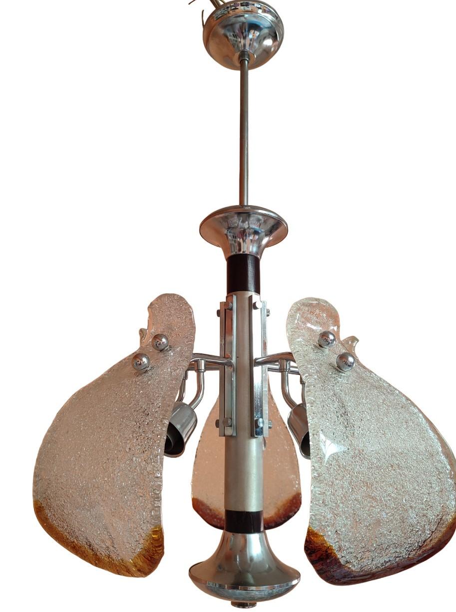 Il lampadario è un esempio affascinante di arte vetraria di Murano prodotto negli anni '70 dalla rinomata ditta Mazzega. Questo lampadario incarna l'eleganza e la maestria artigianale tipica delle creazioni in vetro di Murano, unite alla modernità