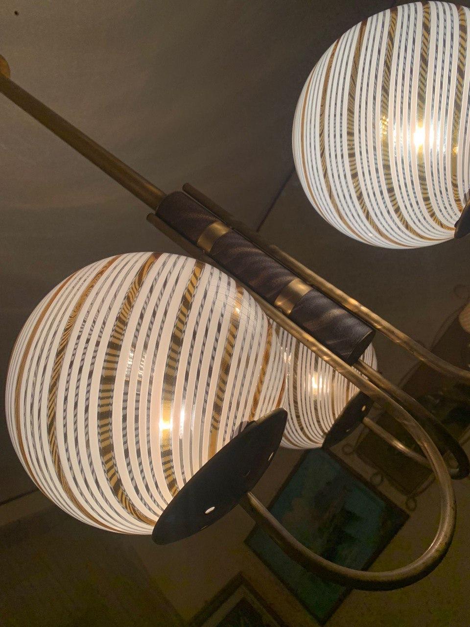 Bellissimo lampadario a  tre diffusori di luce costituiti da bocce in vetro di Murano  con motivo a filigrana di Venini bianco e giallo con struttura in ottone e ghisa. Perfettamente funzionante ,di ottima fattura.
Qualche dettaglio in più al