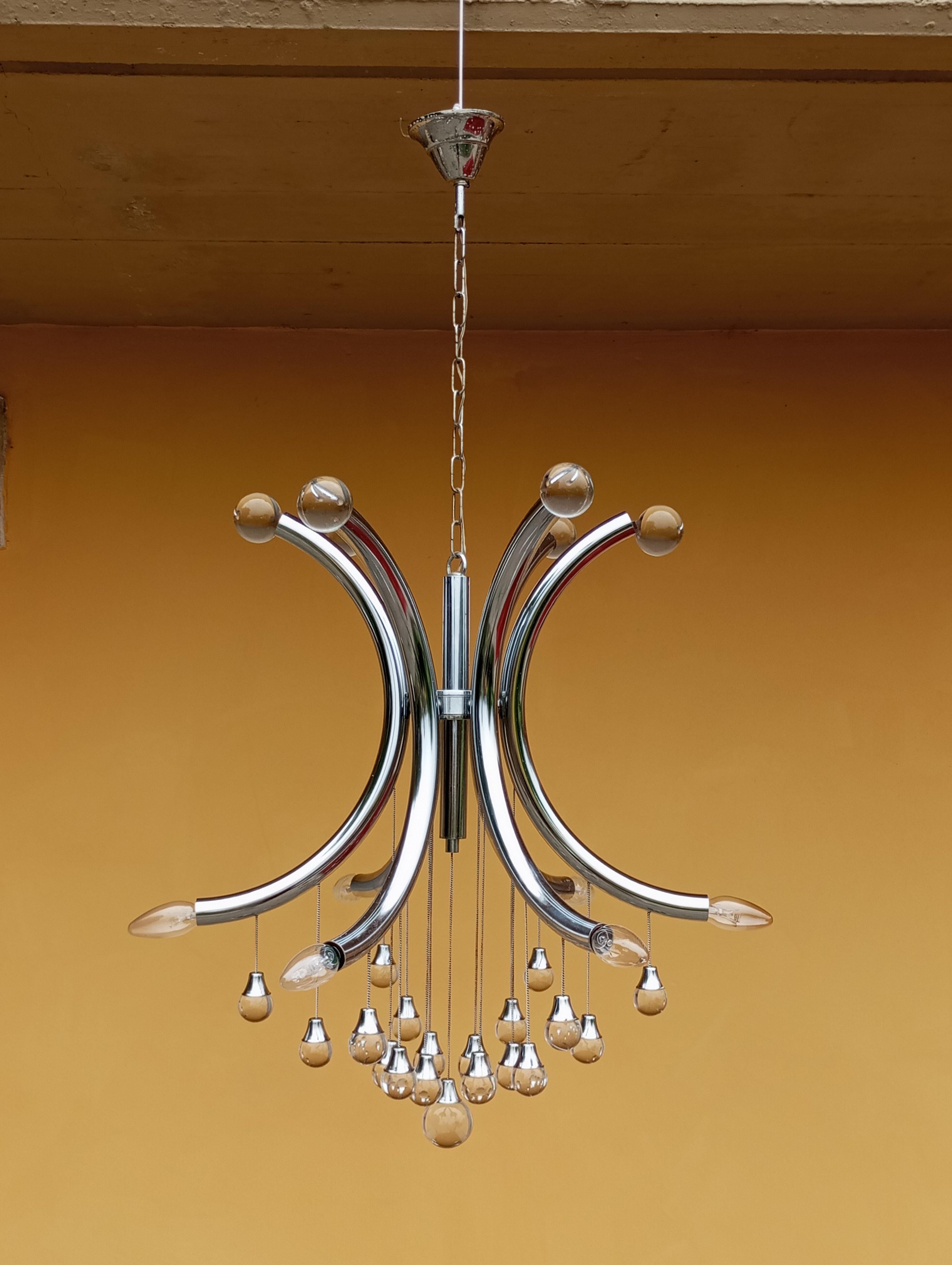 Le lustre de Gaetano Scolari est un exemple raffiné et sophistiqué du design moderne du XXe siècle. La structure centrale se compose d'une base en chrome poli et de six bras incurvés reliés au centre.
À l'extrémité de chacun des six bras se trouvent