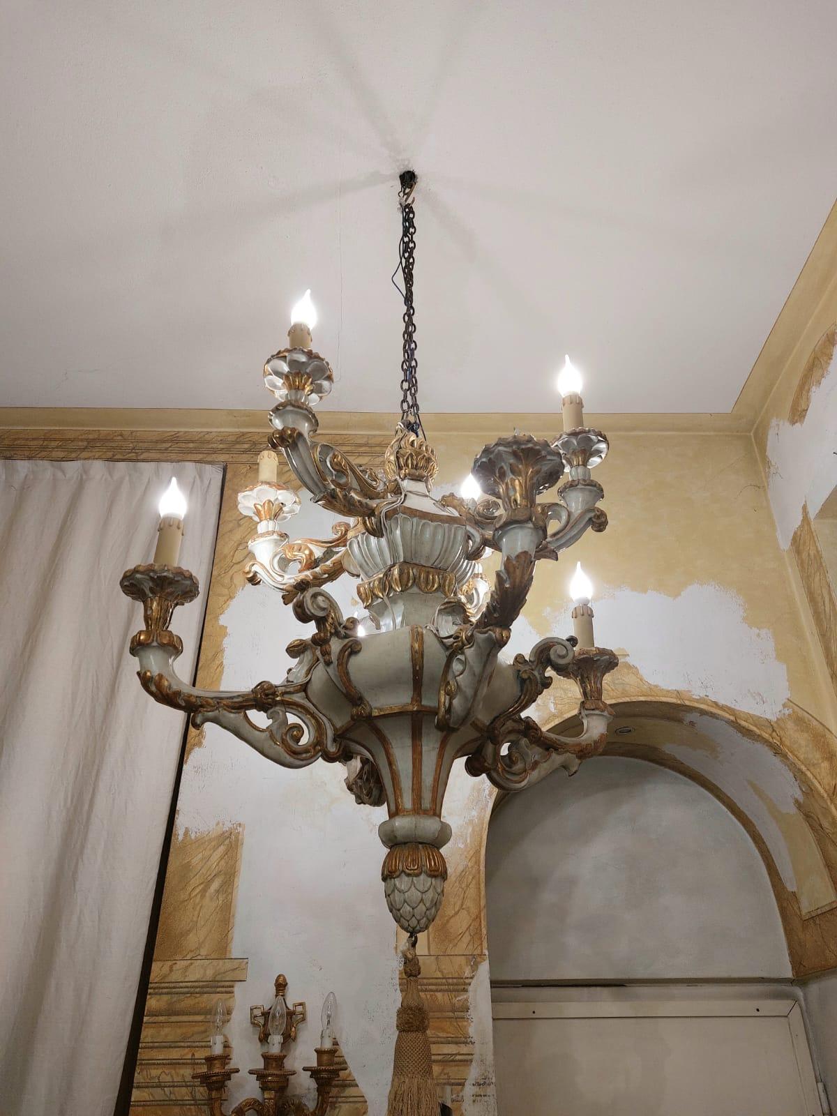 Il lampadario è realizzato in legno laccato color avorio e con profili dorati. Presenta un doppio corpo, con quattro bracci più grandi nella parte inferiore e quattro bracci più piccoli nella parte superiore. Lo stile è Restaurazione, ovvero