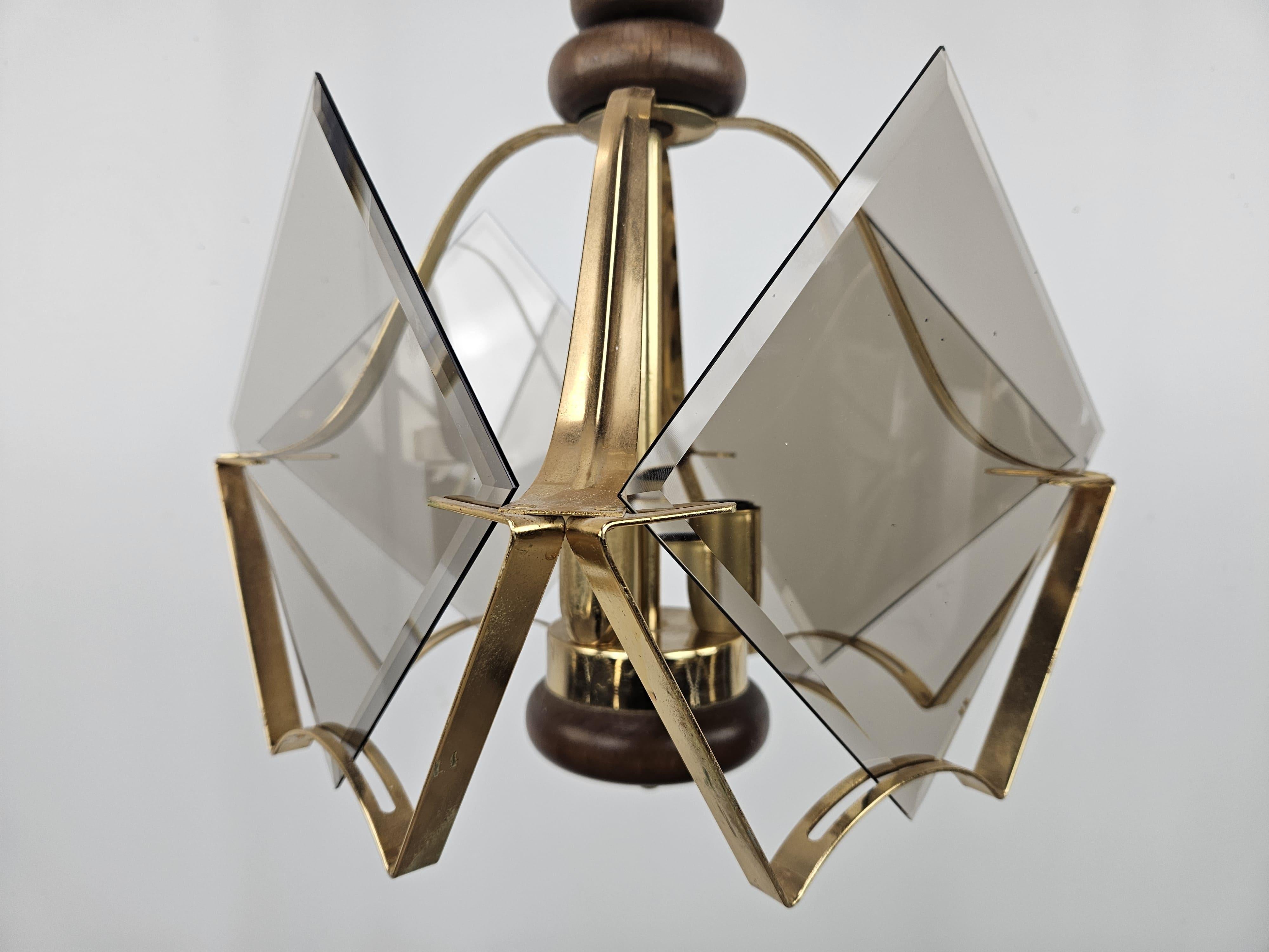 Lampadario vintage in legno e ottone con quattro paralumi laterali in vetro fumè ad incastro, posti a coprire i tre punti luce.

Impianto elettrico originale dell'epoca, consigliata la sostituzione.