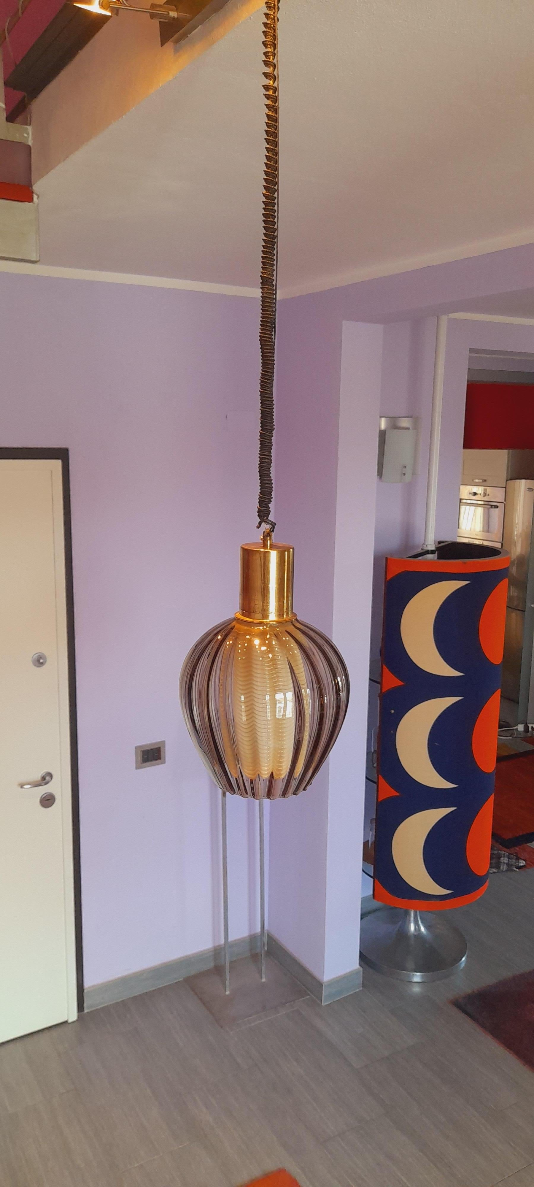 Lampadario realizzato in vetro di Murano negli anni ’60.
Si presenta con una cupola esterna in vetro ambrato, lavorata con un raffinato andamento mosso che crea giochi di riflessi e ondulazioni luminose. Il bordo inferiore è irregolare, con una