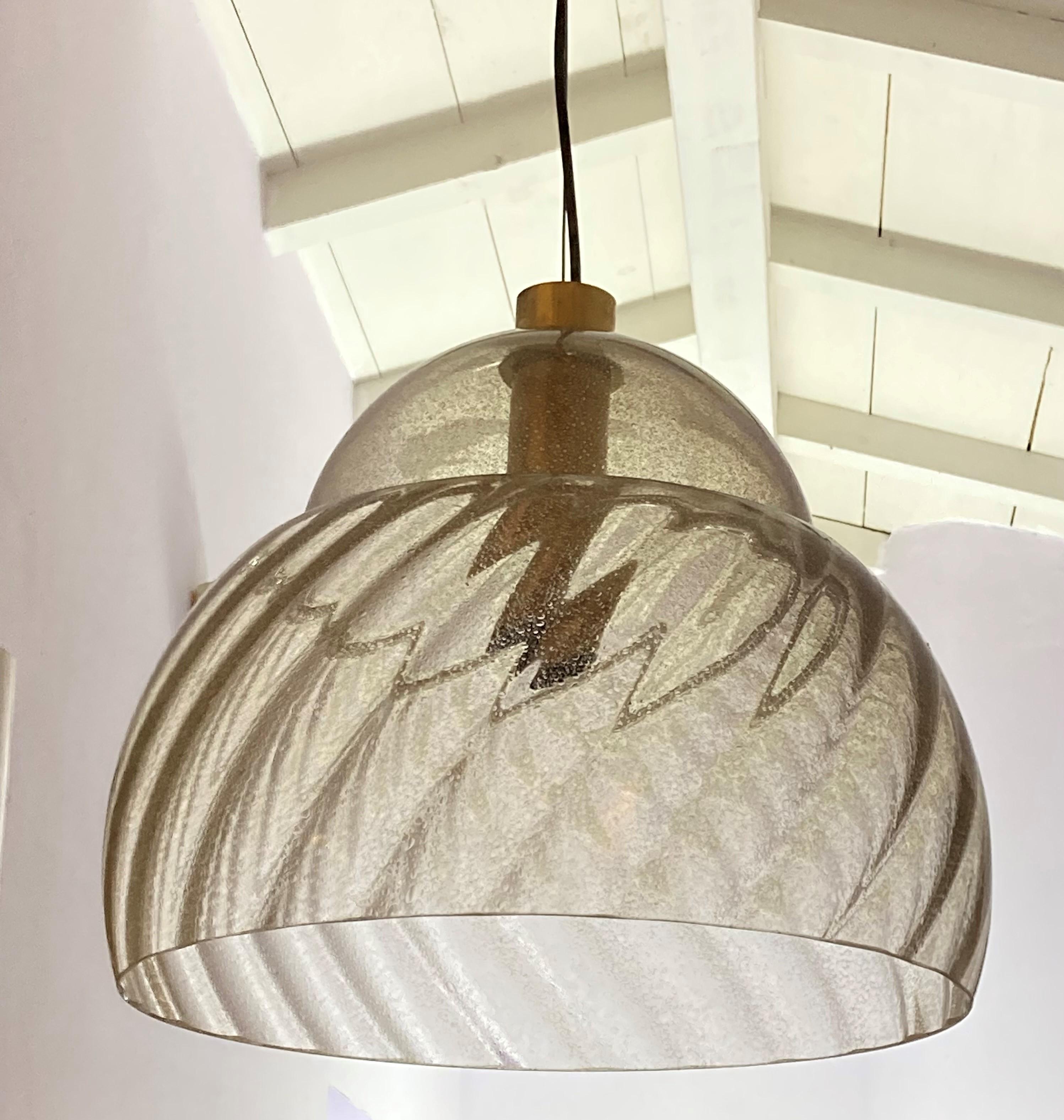  Murano glass chandelier, produced by Mazzega in the 1970s represents the craftsmanship and distinctive design of this period. Made from amber-colored bulicant glass, it presents a combination of shapes that lend a sophisticated, retro