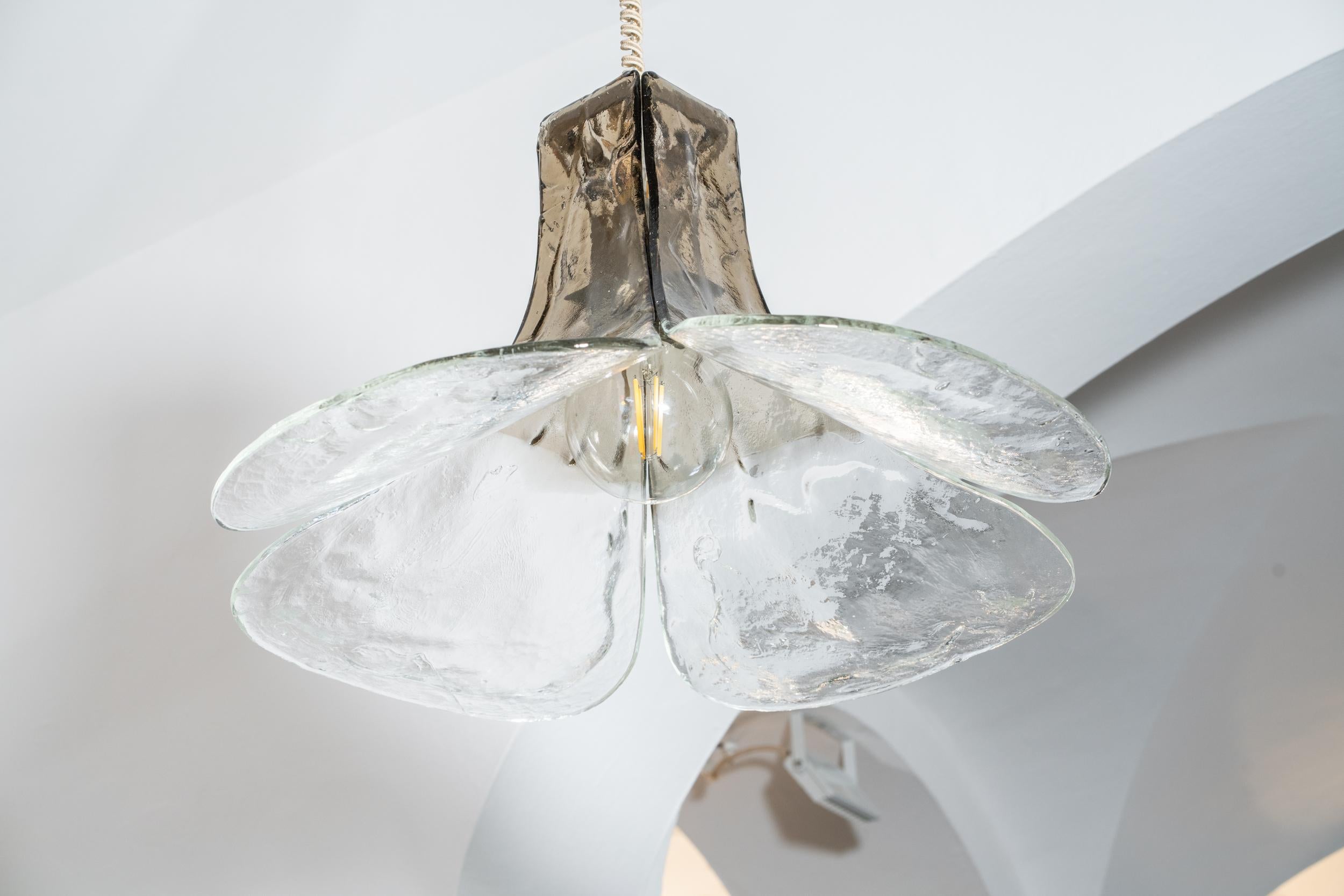 Große Pendelleuchte aus Muranoglas
Entworfen von Carlo Nason und hergestellt von Mazzega, Modell LS185
Die Leuchte besteht aus vier gearbeiteten Glasblättern, mit Schattierungen von transparent bis grün/grau, die an einem Metallrahmen befestigt sind