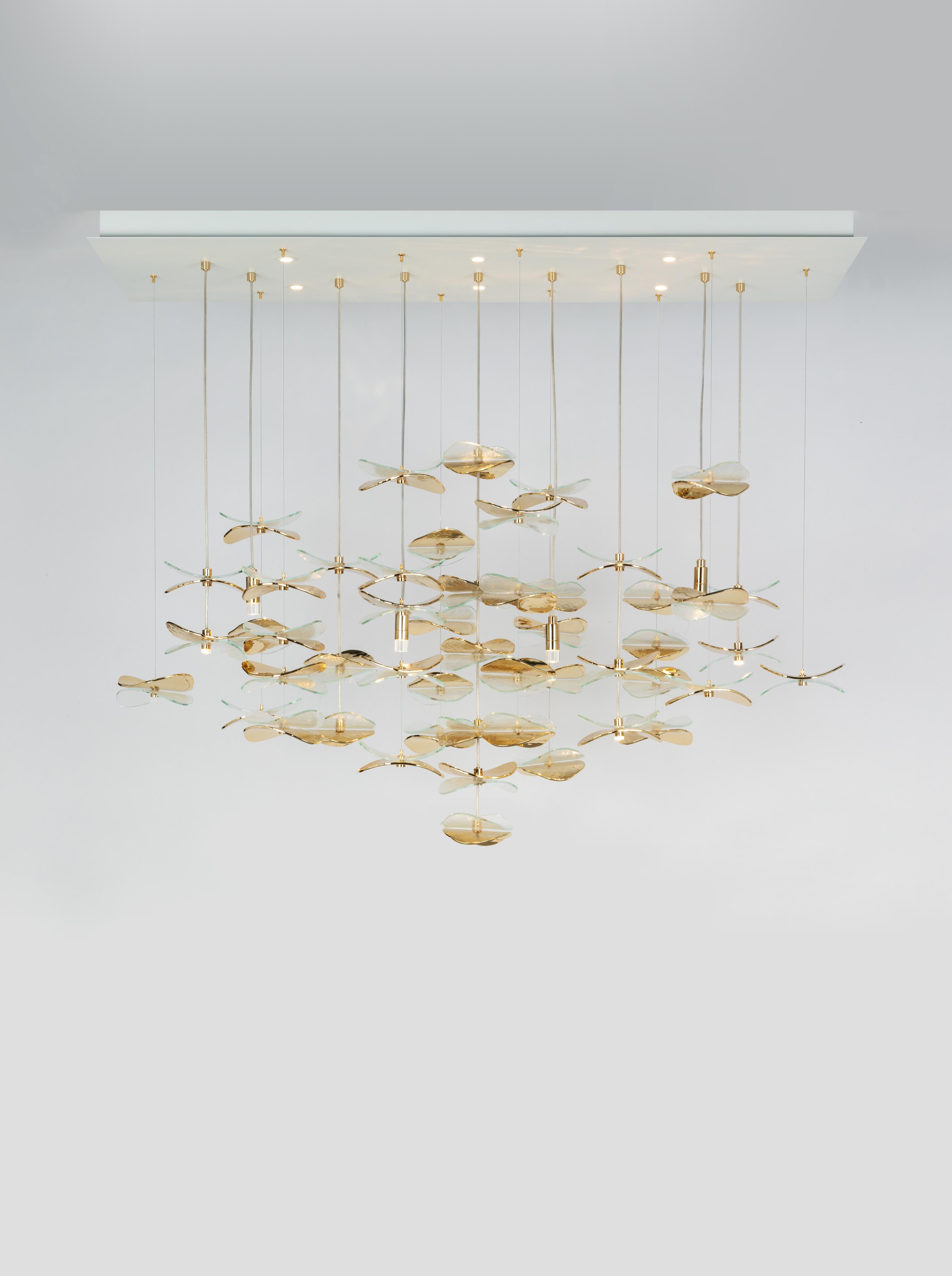 Composizione personalizzabile di petali su cavi elettrici e semplici; i petali sono in vetro trasparente e finitura oro chiaro lucido. Minuteria metallica coordinata; scatola a soffitto in vernice bianca. Disegnato da Lucia Ippolito per Officina