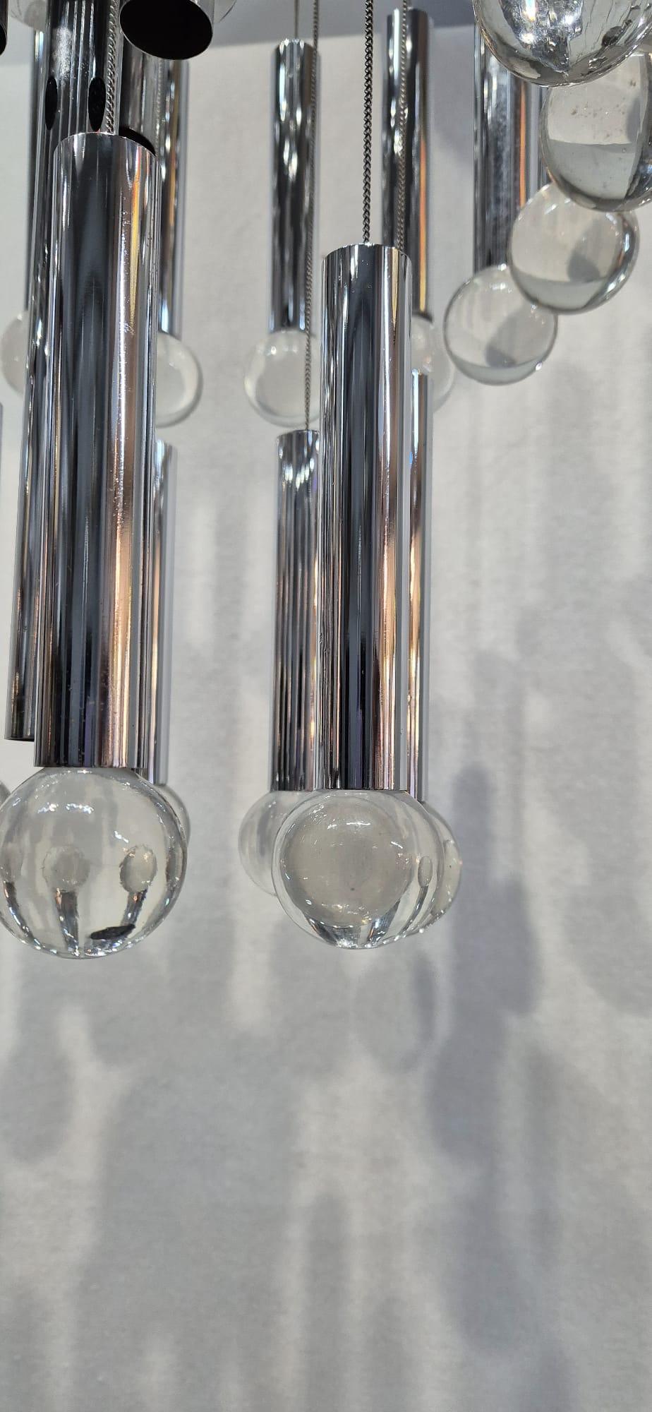 Lámpara Sciolari con estructura de metal y mármoles de cristal de Murano.
Tiene tres niveles, de los cuales el central es el de mayor diámetro. Tiene tres puntos de luz que apuntan hacia arriba y cuatro hacia abajo, para proporcionar a la habitación