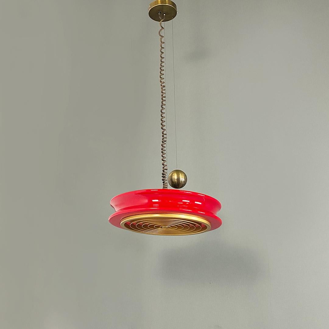 Lampadario modello Orion, a sospensione con contrappeso in ottone di forma sferica, diffusore in vetro rosso dalla forma circolare e sagomato sul profilo ed infine griglia in plastica dorata con disegno concentrico, posta nella parte