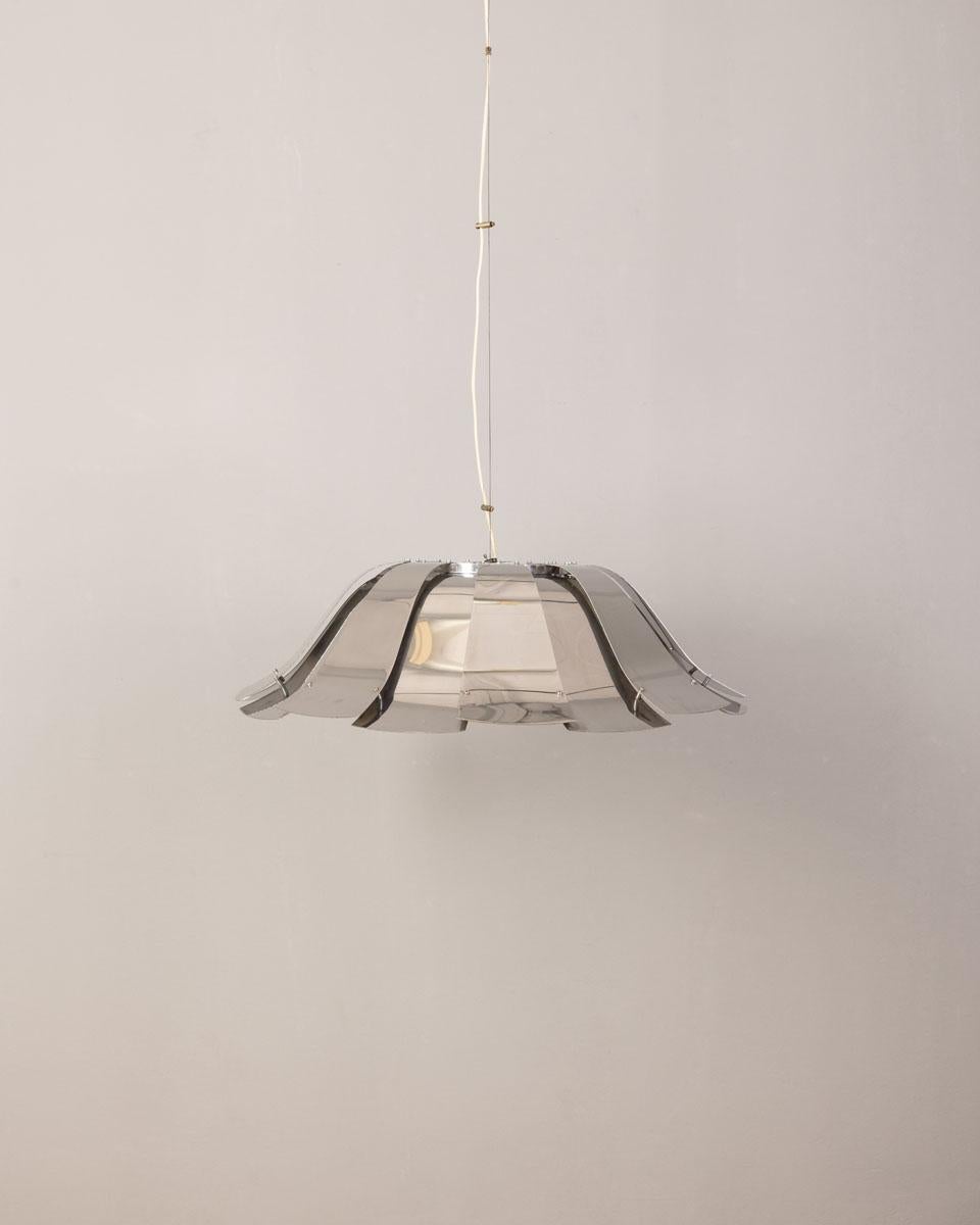 Lampadario con elementi in metallo cromato, sul fondo un paralume laccato bianco, presenta tre luci interne al paralume ed una luce esterna, l'altezza è regolabile. Modello 
