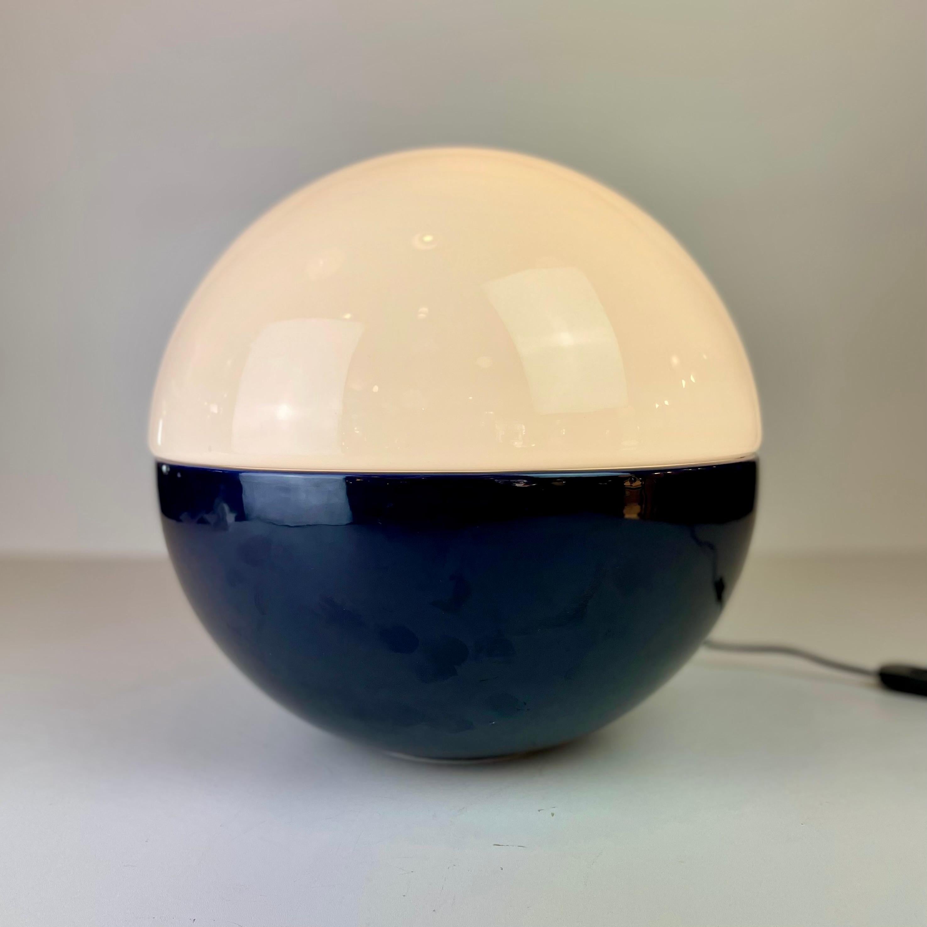 A rare Space-Age table lamp, named Lampalla and made in blown white Murano opalin glass, placed on a deep blue ceramic bowl, this half & half sphere was designed in the 1970’s by Alvino Bagni the Italian designer and editor.
-
Lampe de table rare de