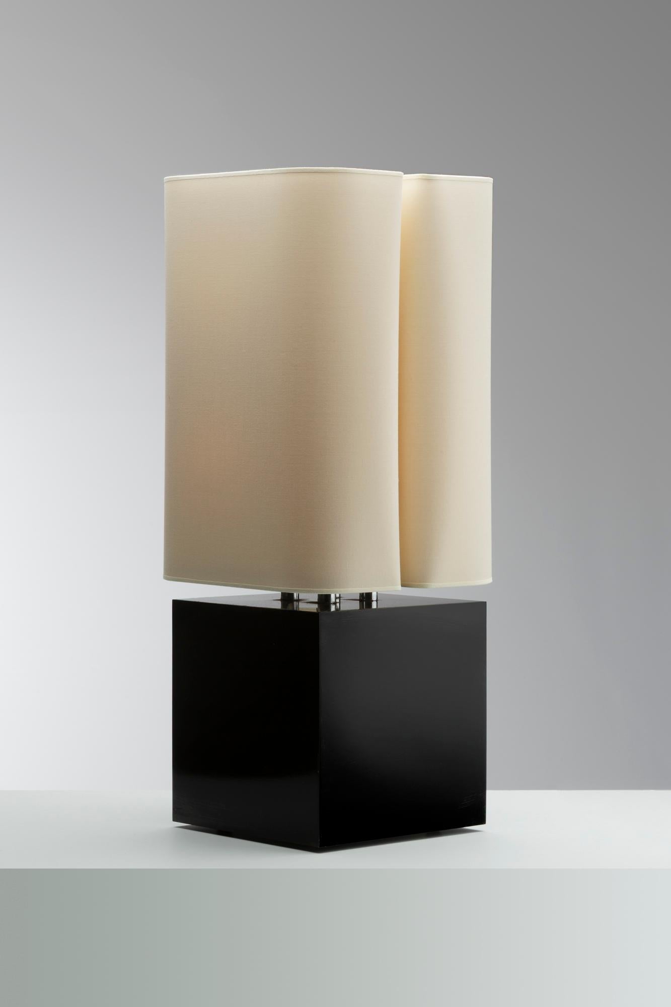 This table lamp by Michel Boyer reflects the refined modernism of his designs from the late 1960s and 1970s. Resting on a solid cubic base in lacquered black wood, the lamp is crowned by a pair of gently curved, cylindrical fabric shades. The