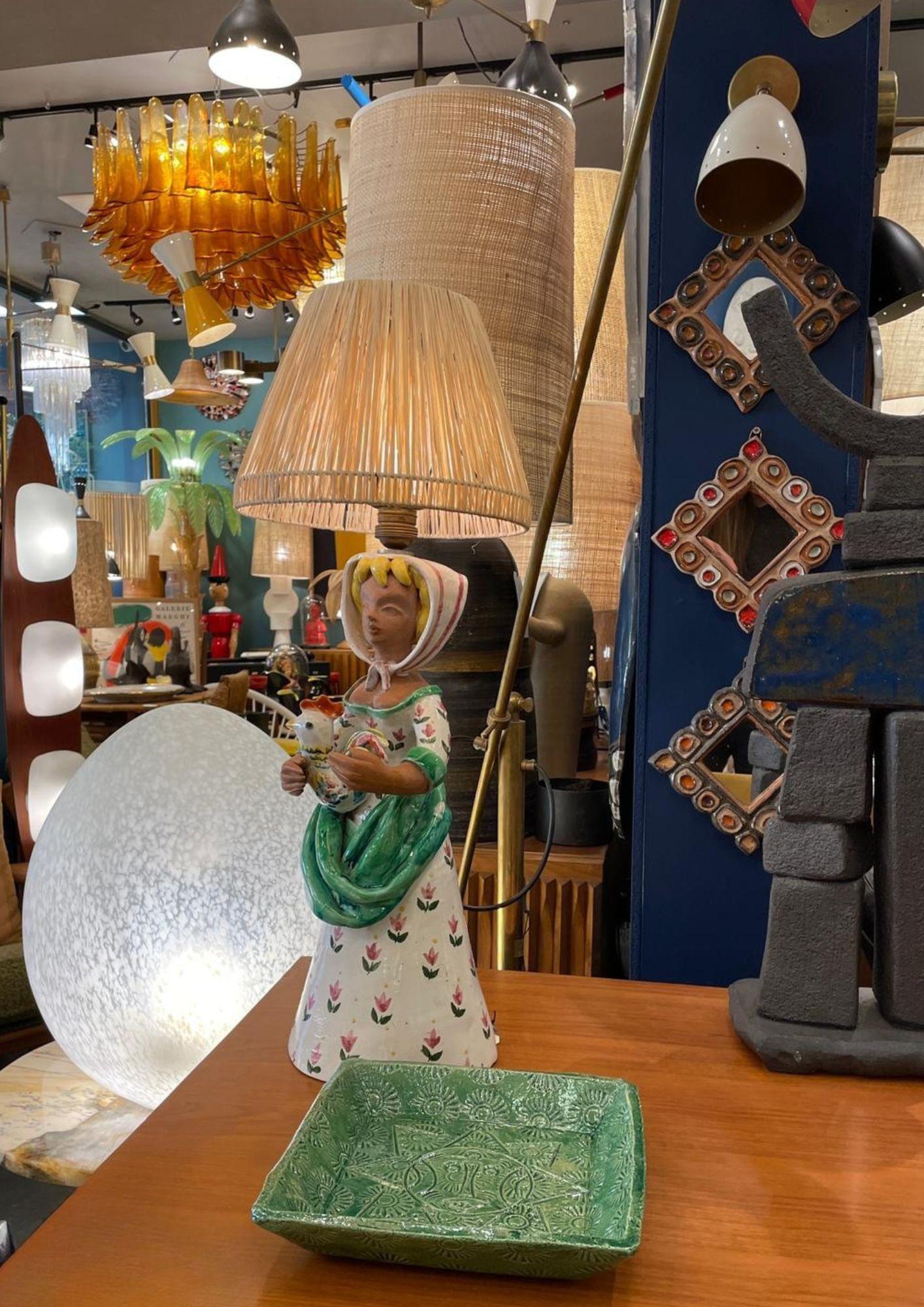 Lampe de table avec base en céramique émaillée représentant une femme tenant un coq : 65 x 18 cm y compris l'abat-jour 
Design/One 