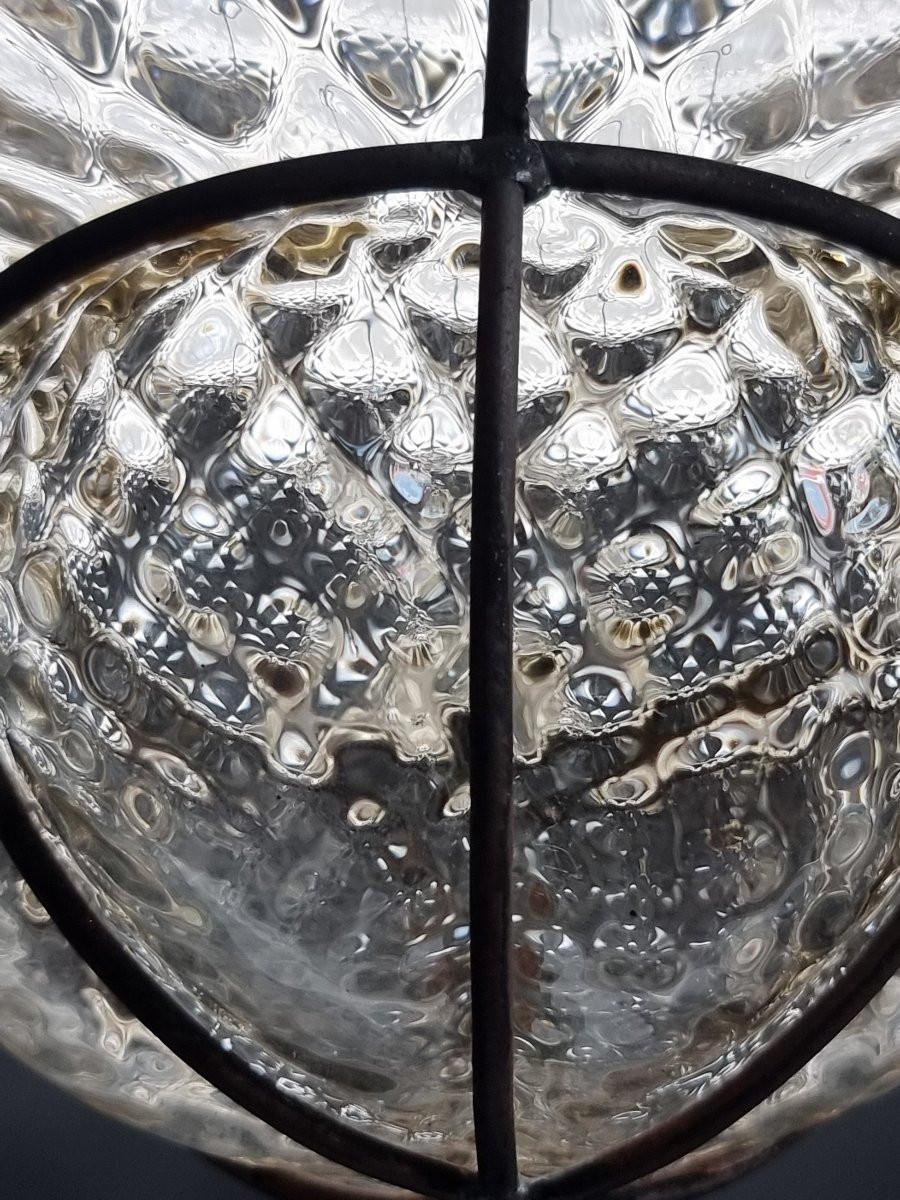 Affascinante lampione veneziano risalente ai primi anni del Novecento, realizzato interamente in vetro soffiato, impreziosito da una raffinata struttura in ferro con motivi decorativi. L’armoniosa combinazione dei materiali, unita alla maestria