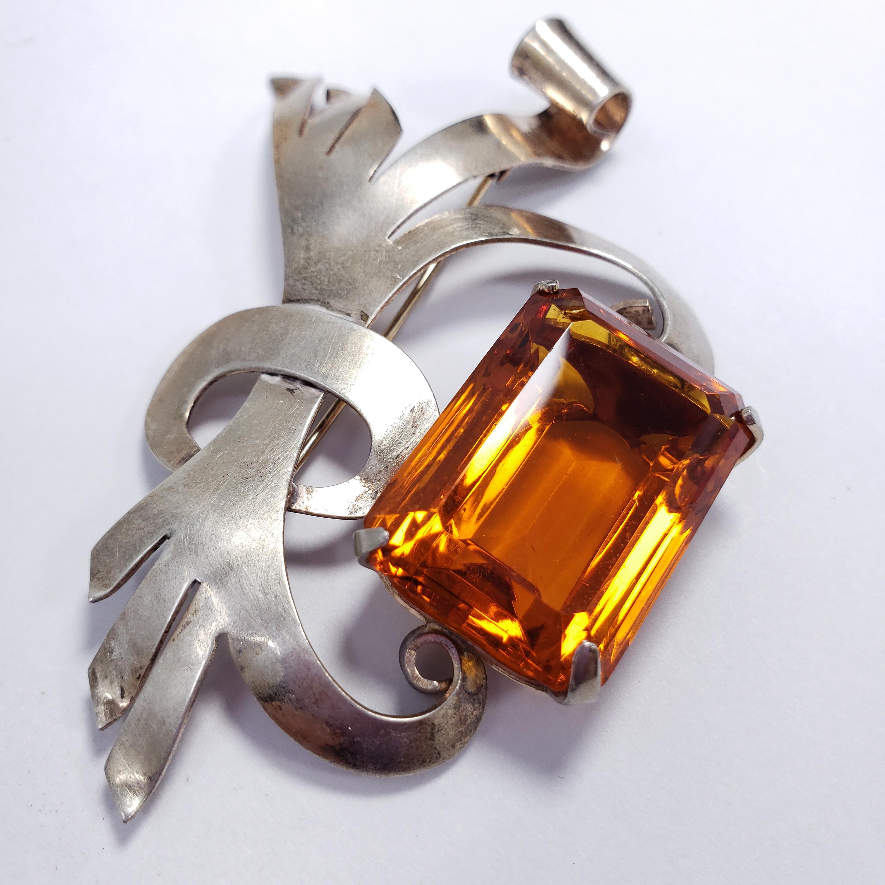 A pin brooch by Lampl. It features a decorative sterling silver bow-like motif, accented with a large emerald cut dark orange crystal. A stylish vintage accessory!

Hallmarks: Sterling, Lampl