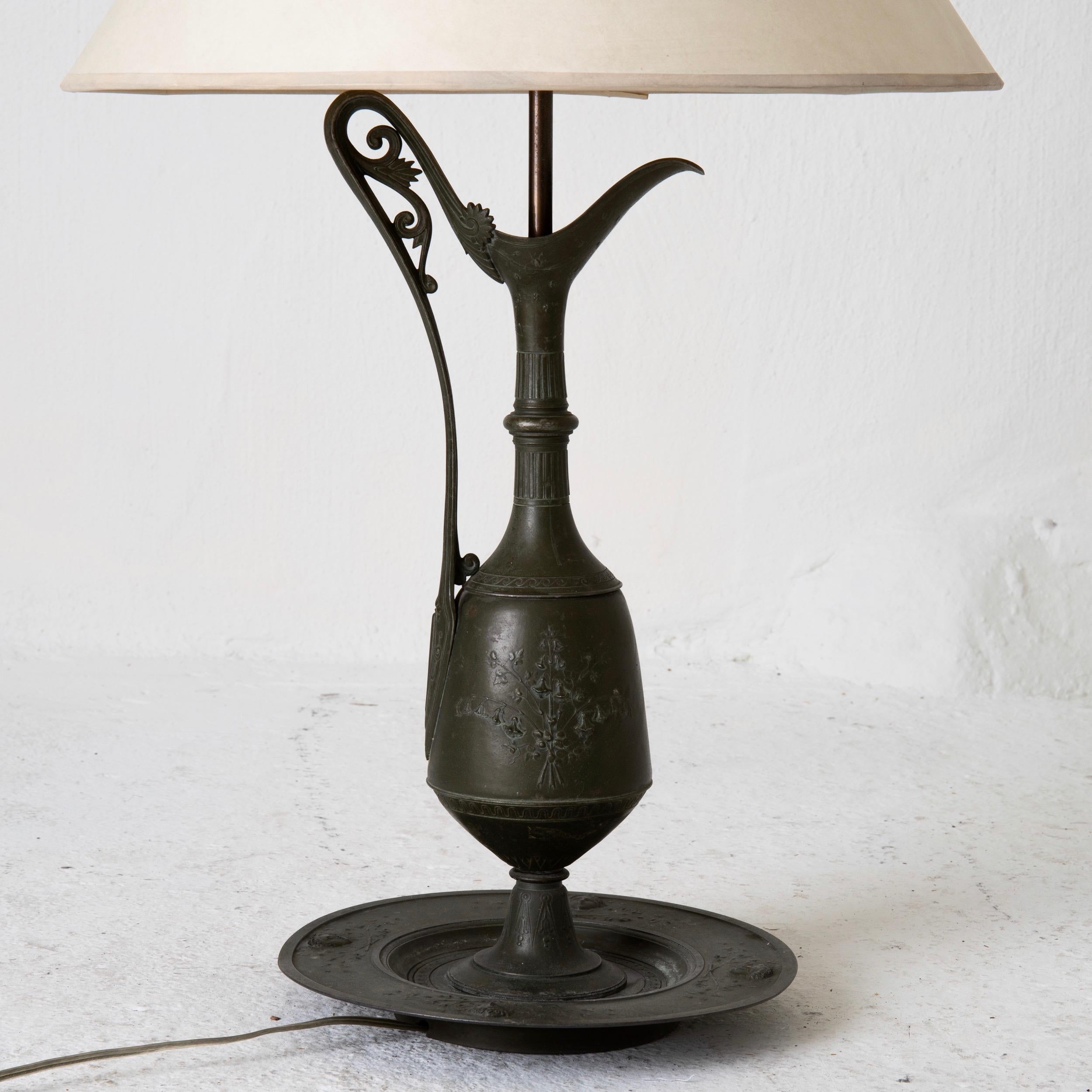 A pair of table lamps made in the neoclassical style during the early 20th century. Pitcher shaped bases. Dark metal with classical motifs. Cream colored shades.

 
