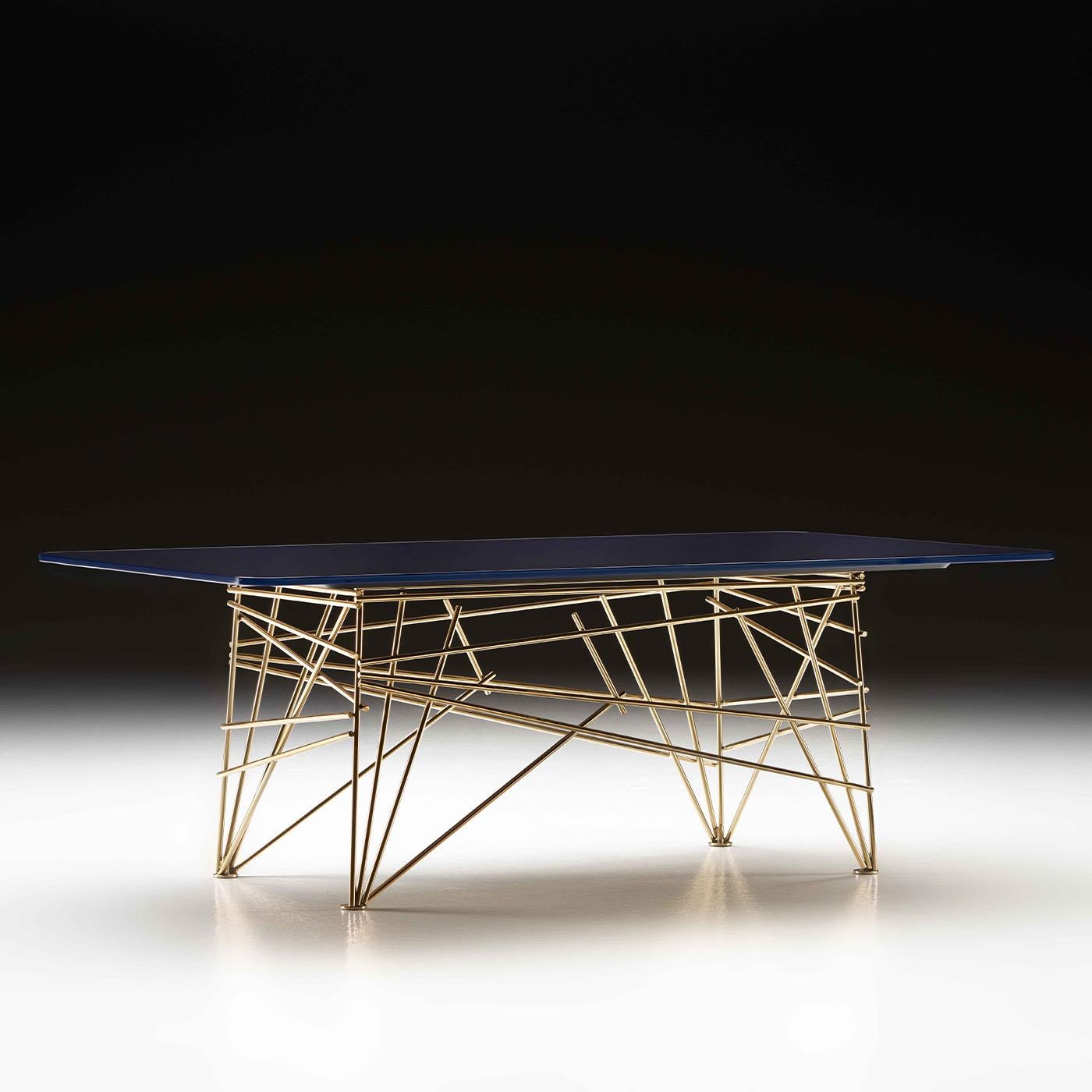 A luminous base where glossy golden stainless steel sticks intricately interact for a stunning dynamic statement that distinguishes this stylish table. The blue shade the glass top is back-painted in suggests a chromatic combination of regal